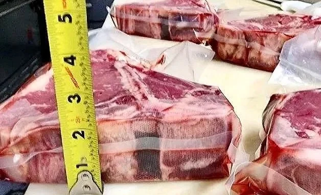 Fresh cuts of beef wrapped in plastic on a butcher's counter, with a measuring tape indicating their size.