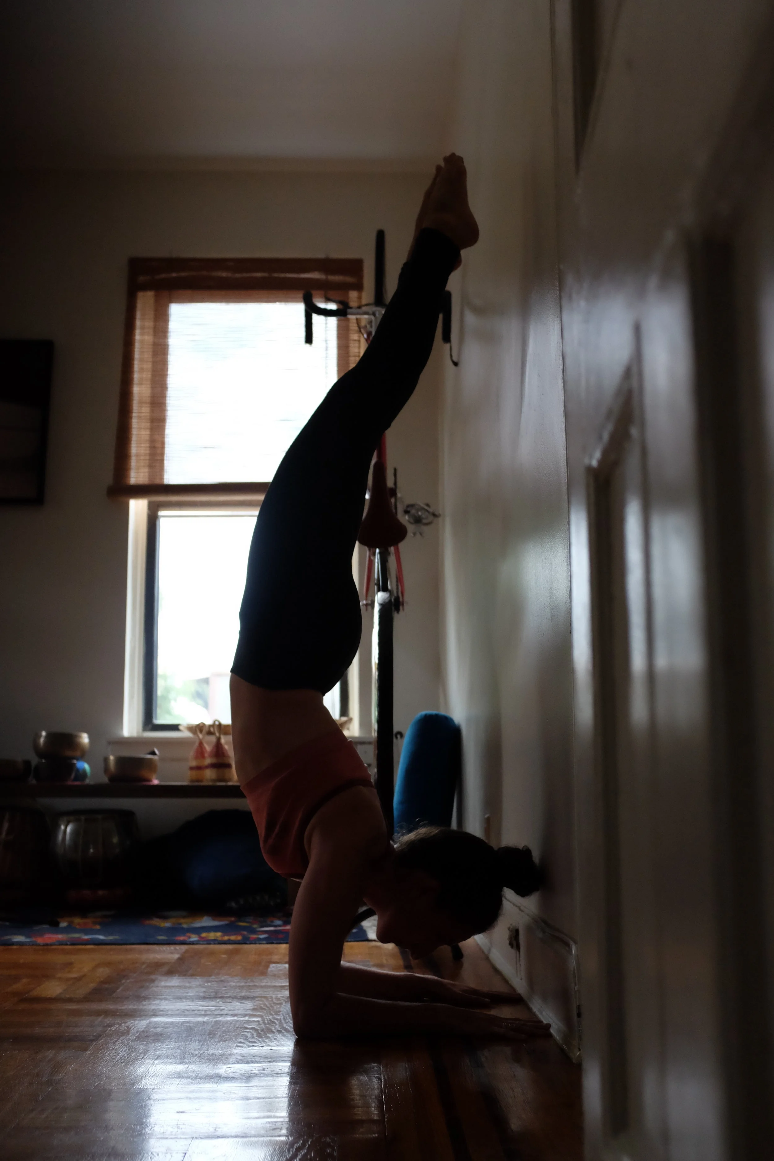 Person performing a headstand against a wall in a living room, with sunlight coming through windows.