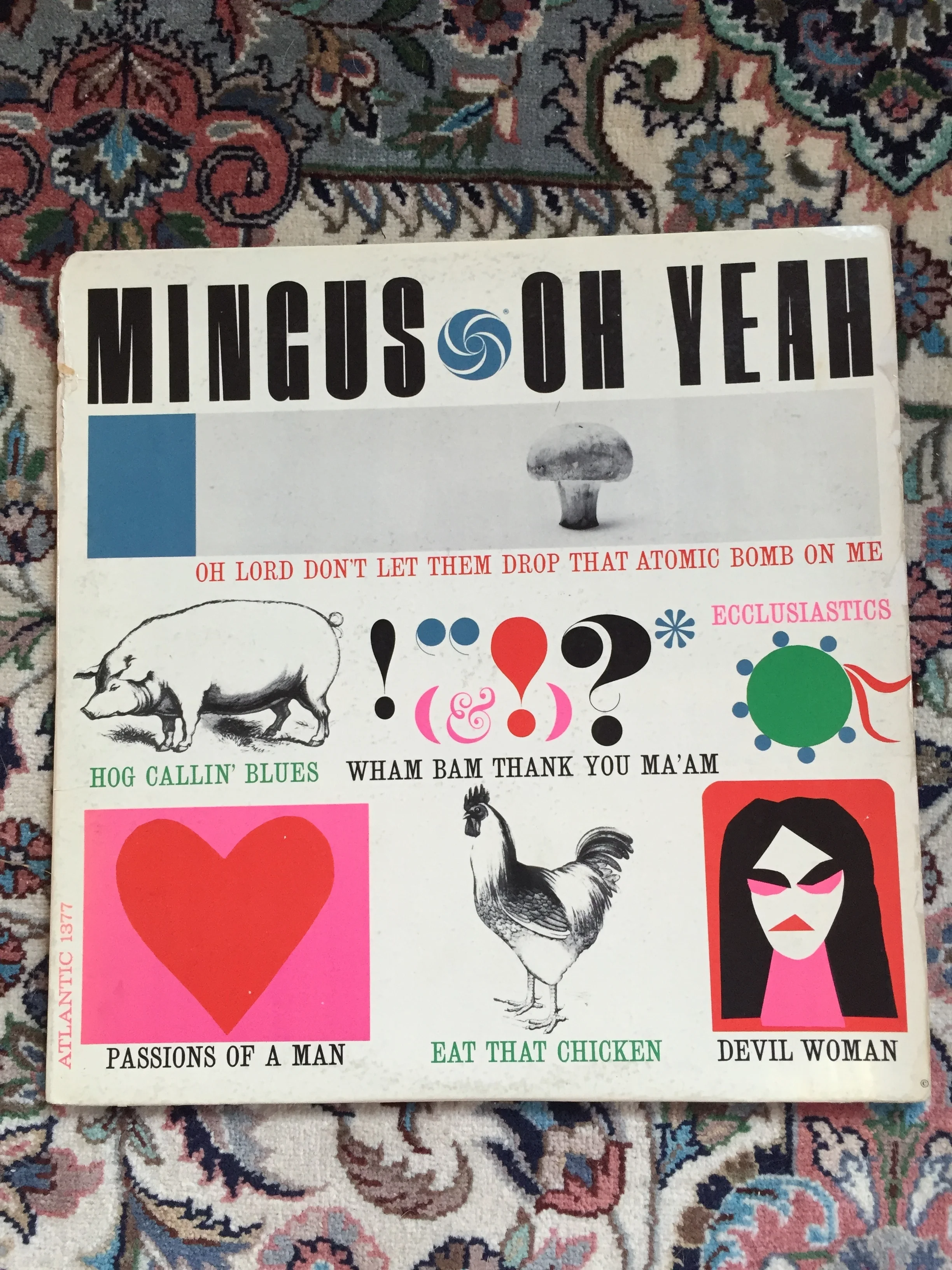 A collage-style illustration with various images and text. The top features the words 'MINGUS OH YEAH' with a blue and white spiral design. Below, a line of red text says, 'OH LORD DON'T LET THEM DROP THAT ATOMIC BOMB ON ME.' Other elements include a