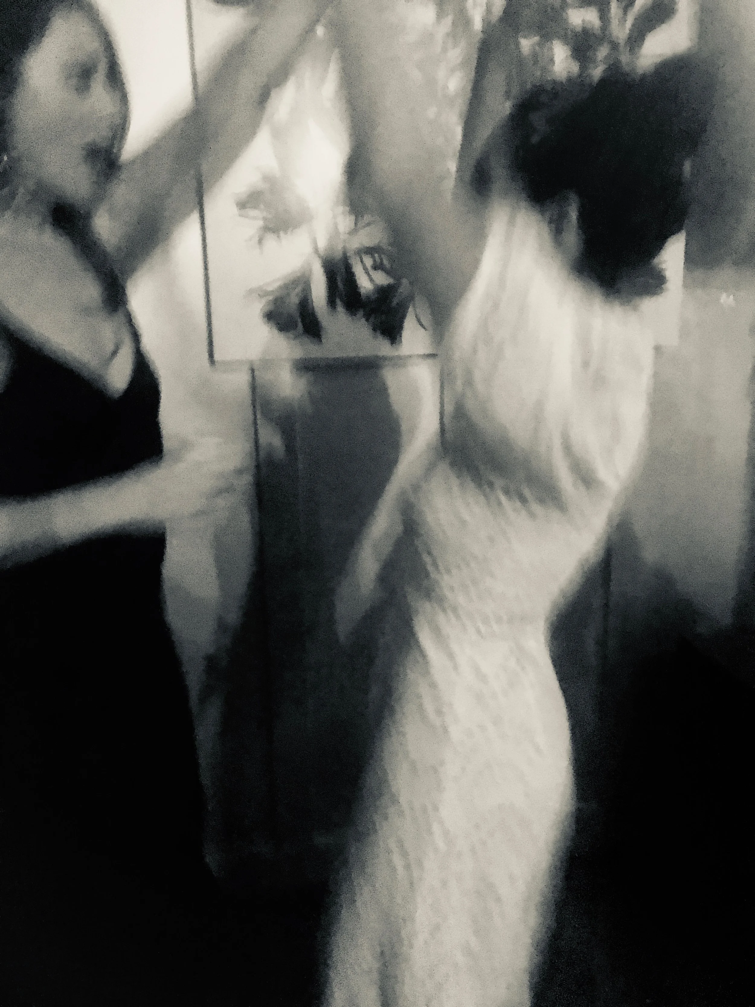 Two women, one in a sleeveless dress with an updo hairstyle and the other in a dark top, are in an art gallery observing abstract paintings on the wall.