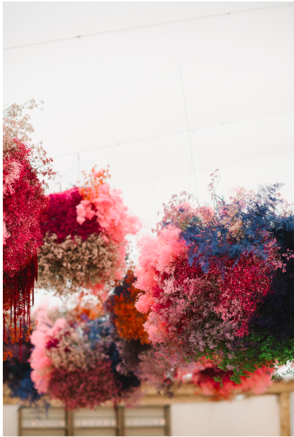 Colorful hanging floral arrangements with pink, red, blue, and purple flowers in an indoor setting.