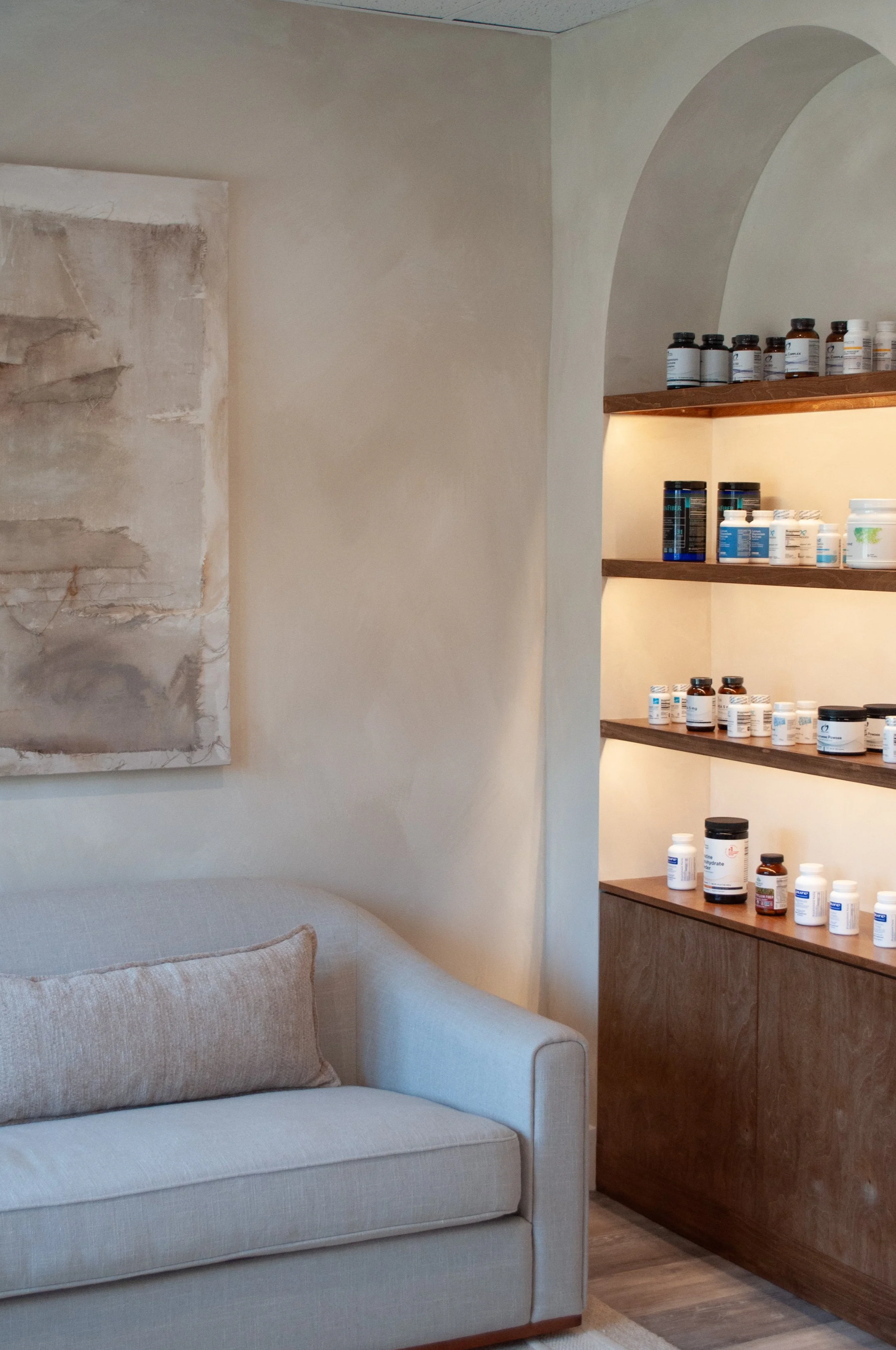 Living room with a white sofa, abstract artwork on the wall, and shelves filled with bottles and containers, possibly supplements or medications.