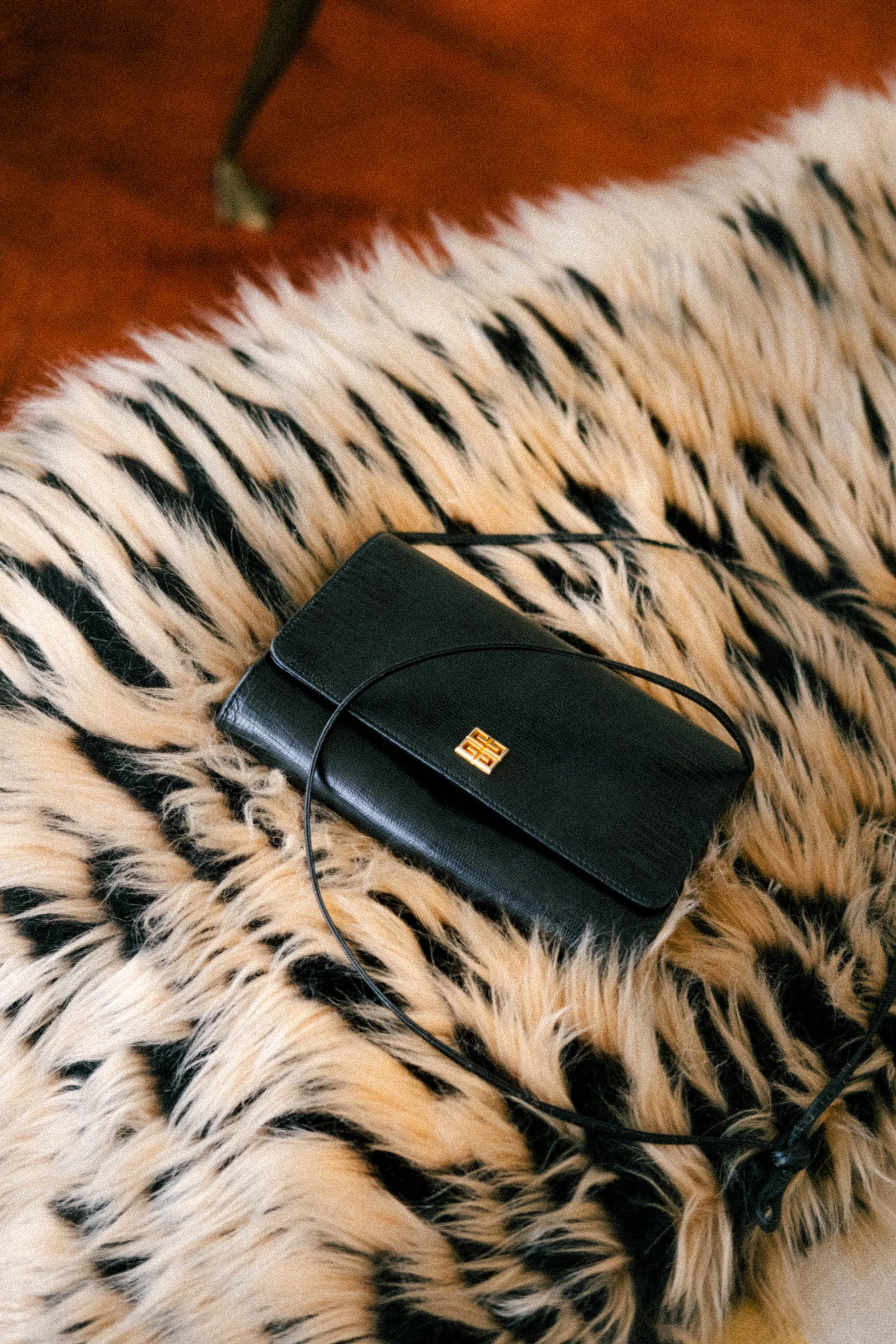 A black handbag with a gold logo resting on a leopard-print faux fur blanket.
