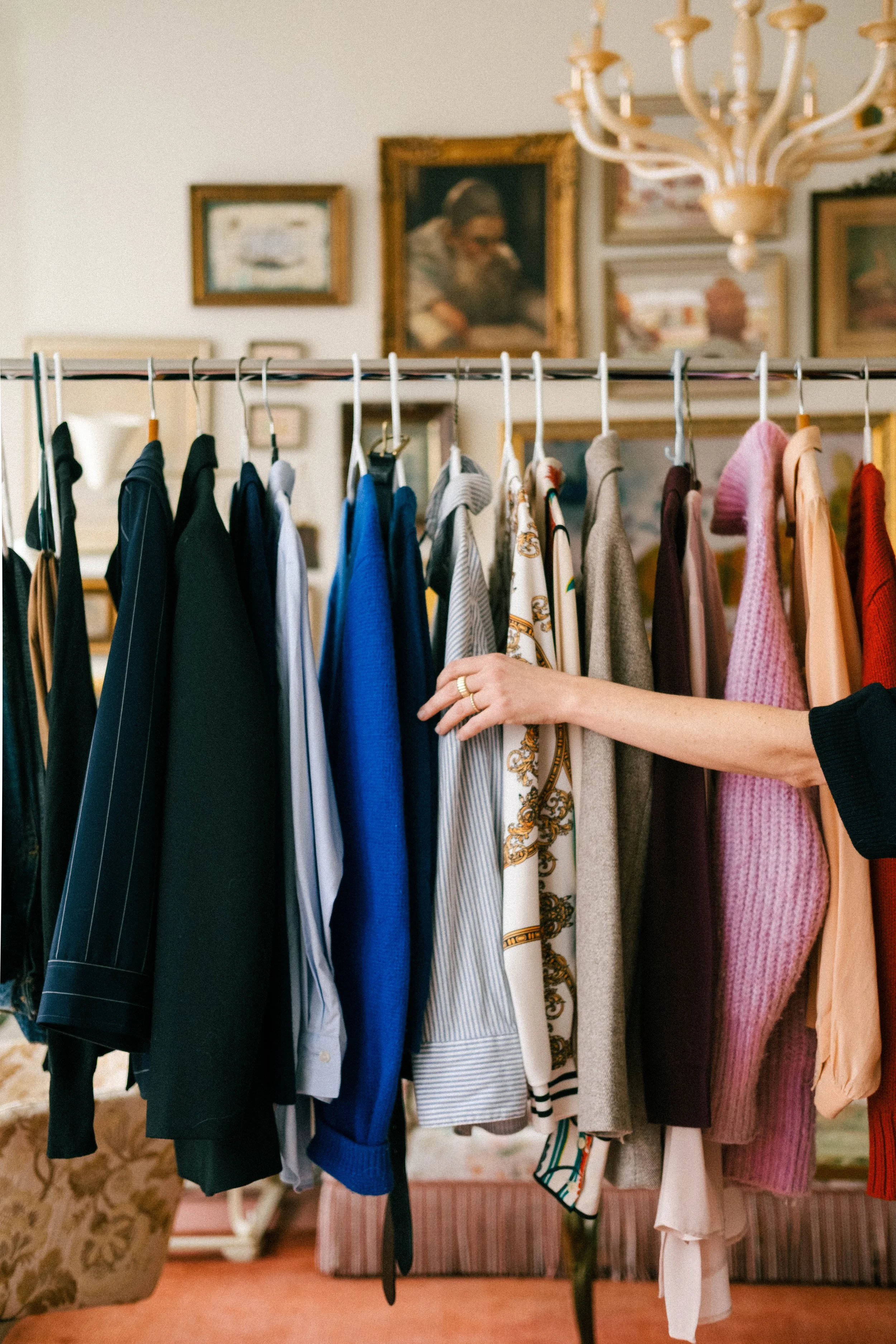 A person browsing a clothing rack with various shirts, sweaters, and jackets in a vintage-style room.