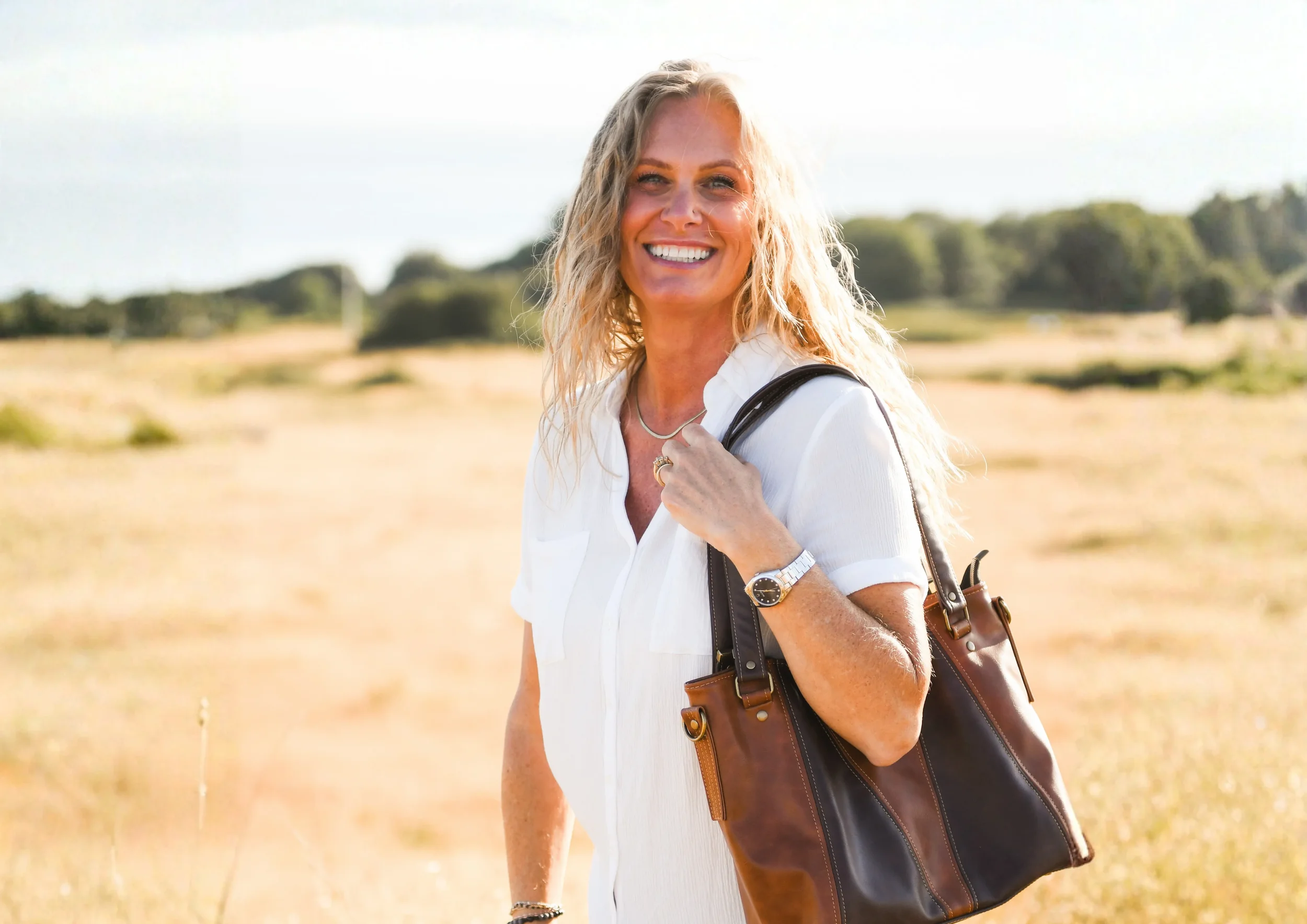 Stacey holding a brown shoulder bag and smiling