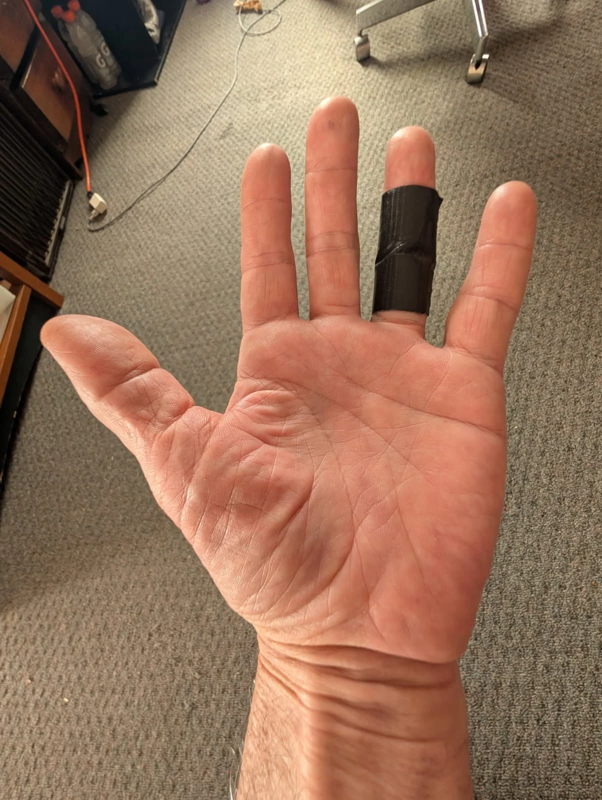 A man's strong hand palm up fingers spread with a black bandage on the ring finger