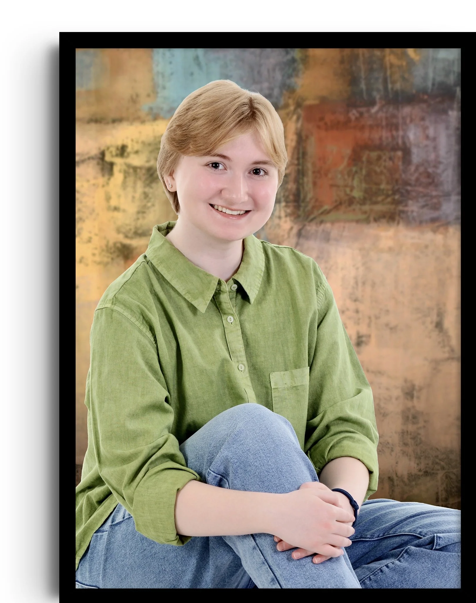 Portrait of a young woman with short light brown hair, wearing a green button-up shirt and blue jeans, sitting with her arms crossed and smiling, with an abstract multicolored background.