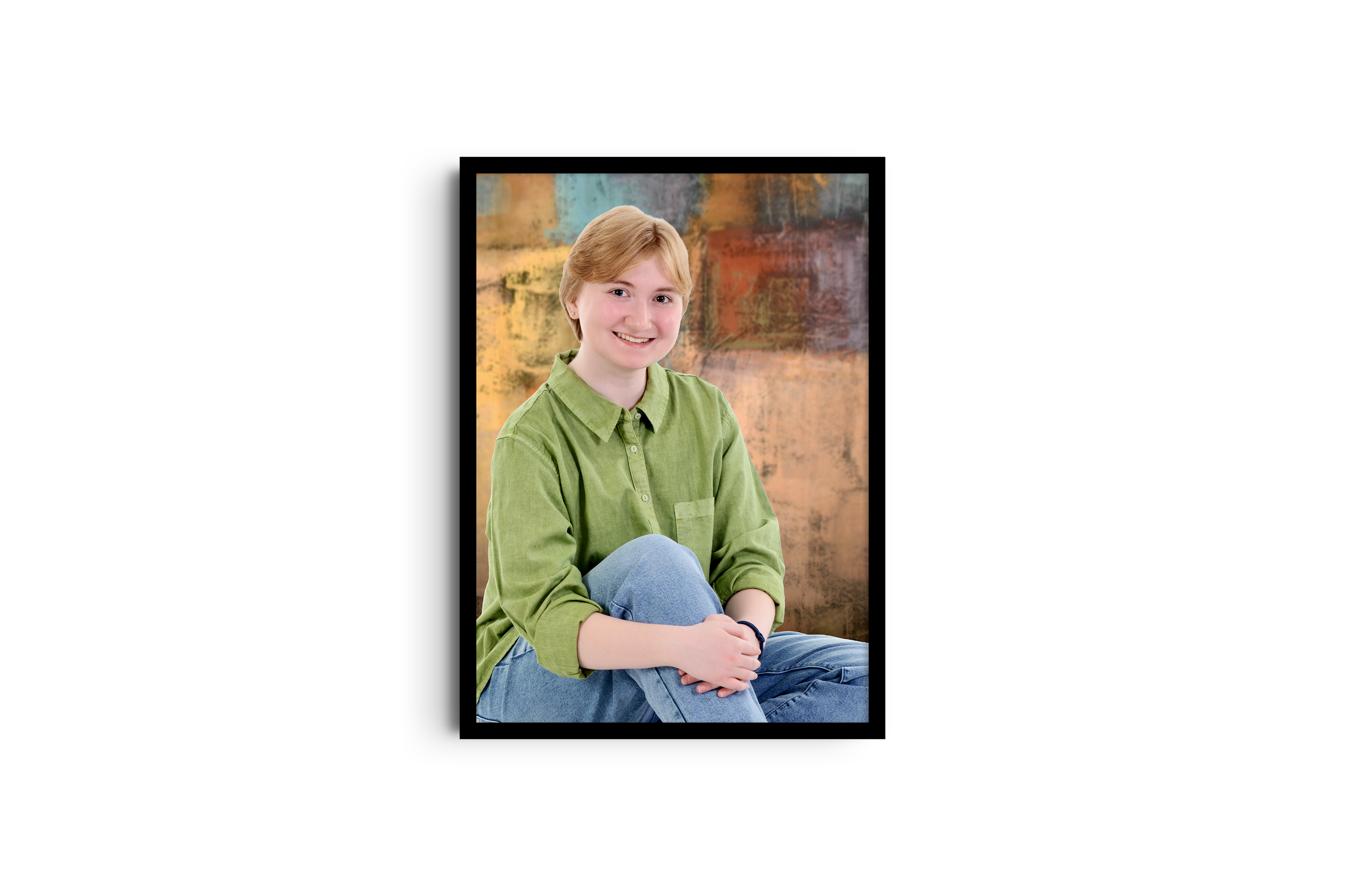 A young person with short blond hair wearing a green shirt and blue jeans, sitting with one knee up against a multicolored textured background.