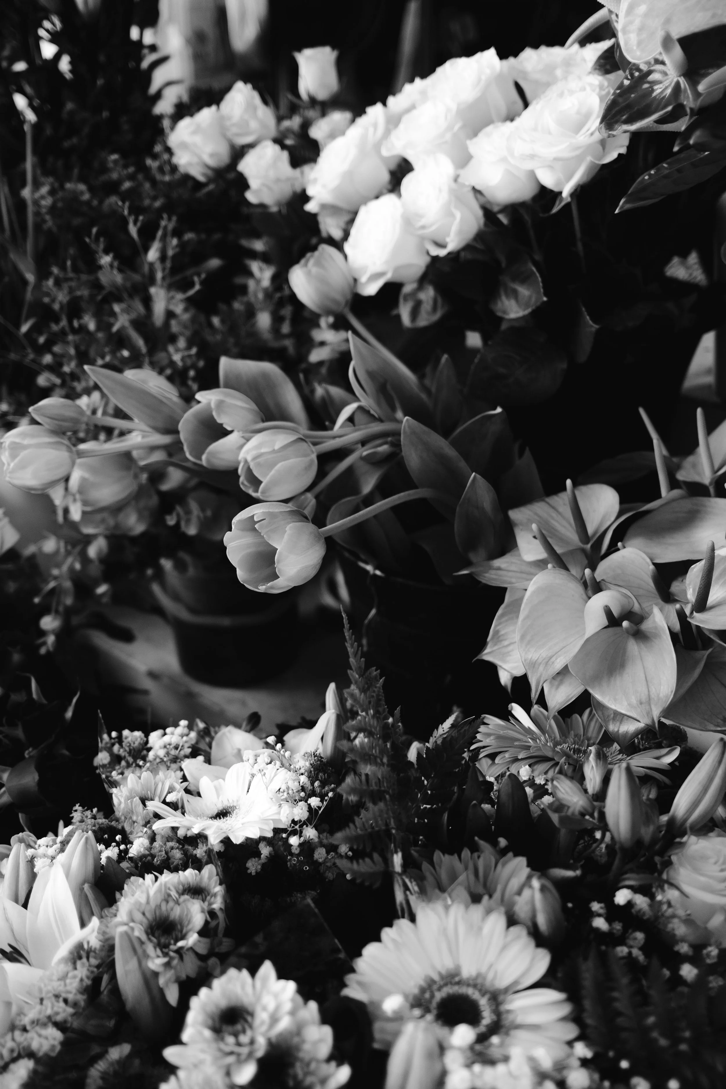 Black and white photo of various flowers including roses, tulips, and daisies arranged as a bouquet or floral display.