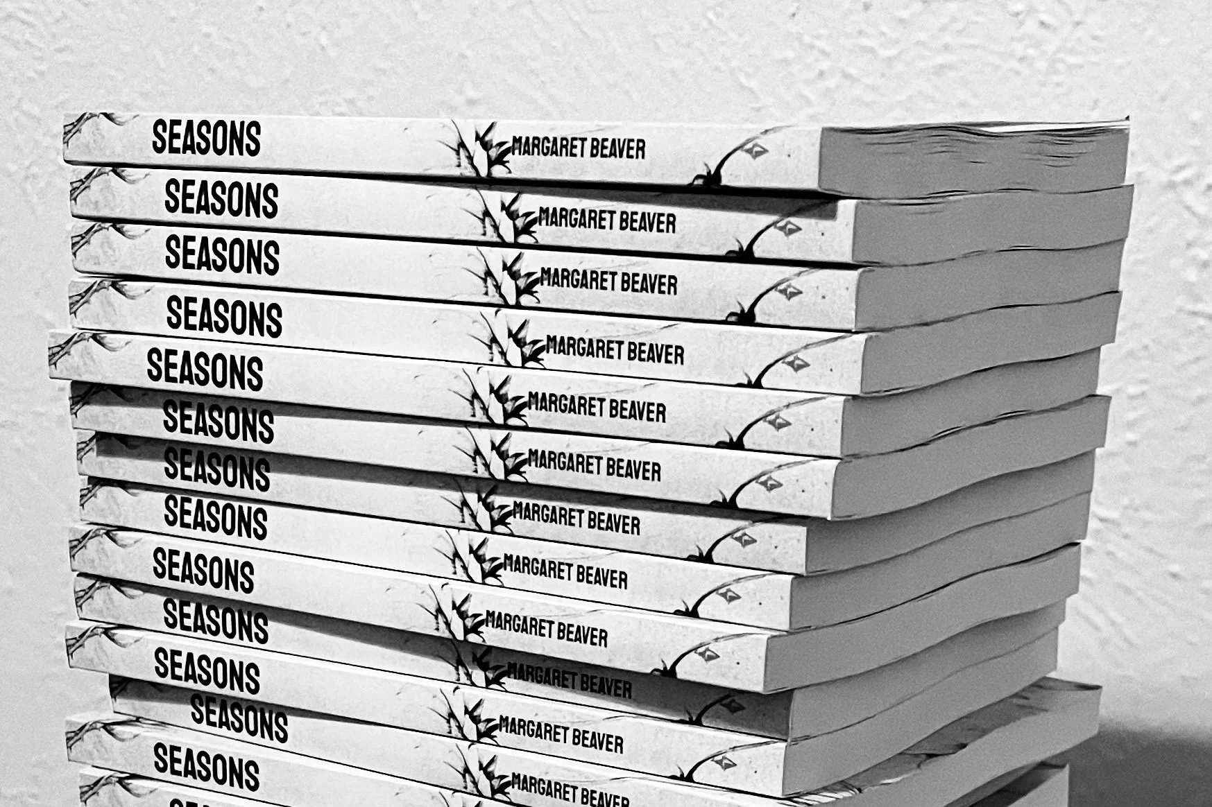Stack of multiple copies of the book titled 'Seasons' by Margaret Beaver with a bamboo and leaf design on the cover.