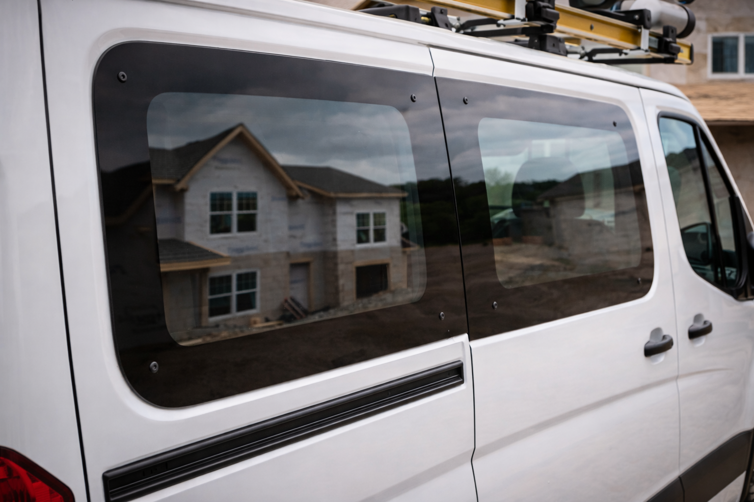 Reflected image of a house with a gabled roof in the windows of a white van