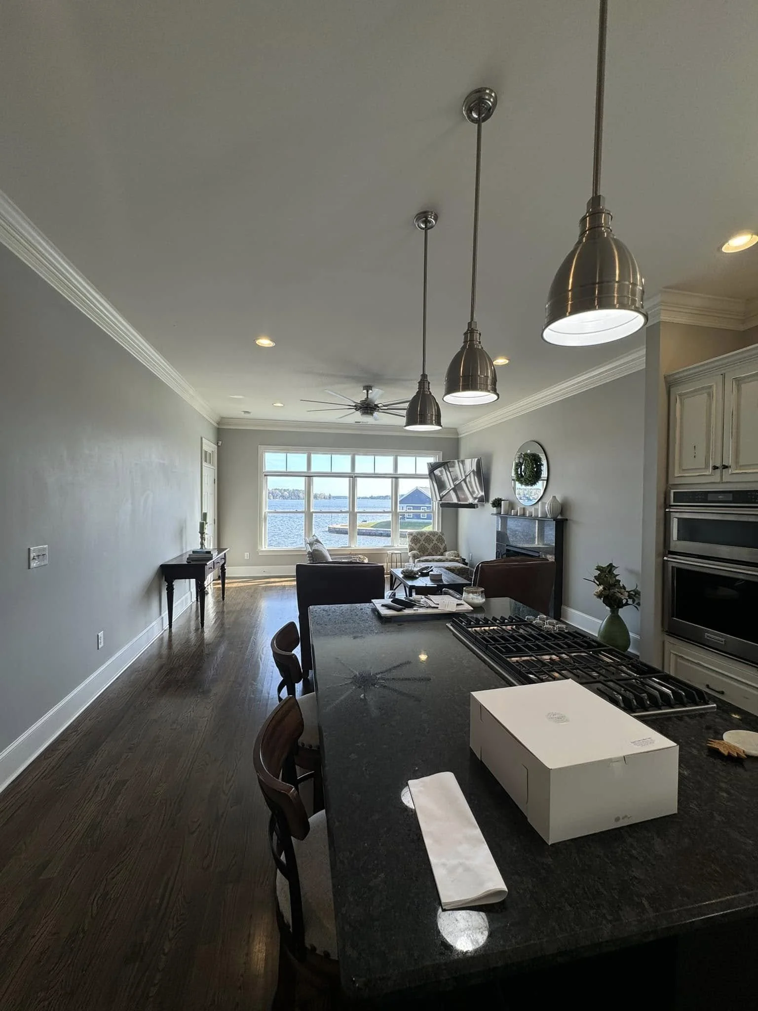 Open-concept living and kitchen area with large window view of a water body, pendant lights above kitchen island, and modern decor.