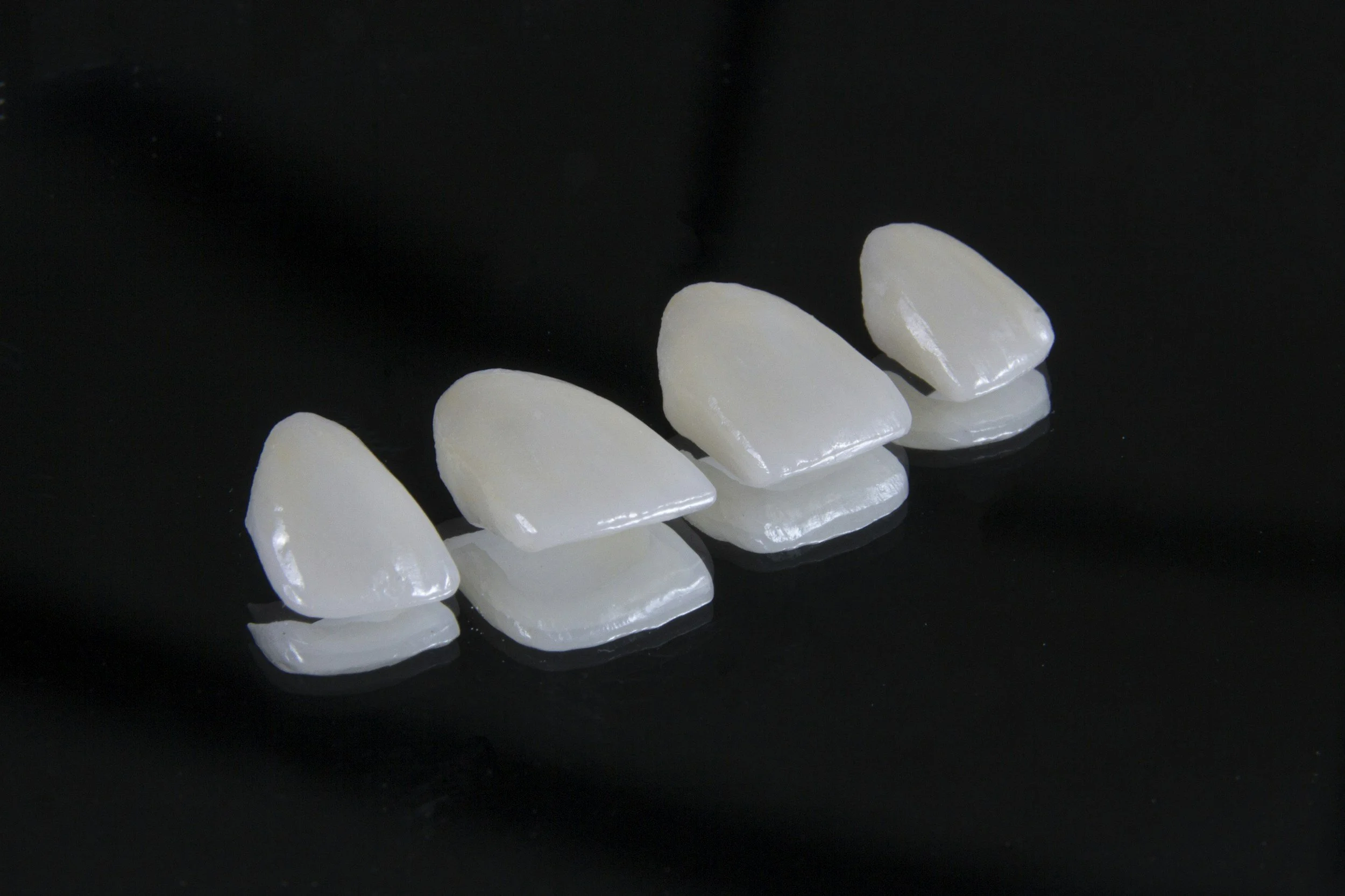 Multiple white, dental veneers or crowns on a black reflective surface.