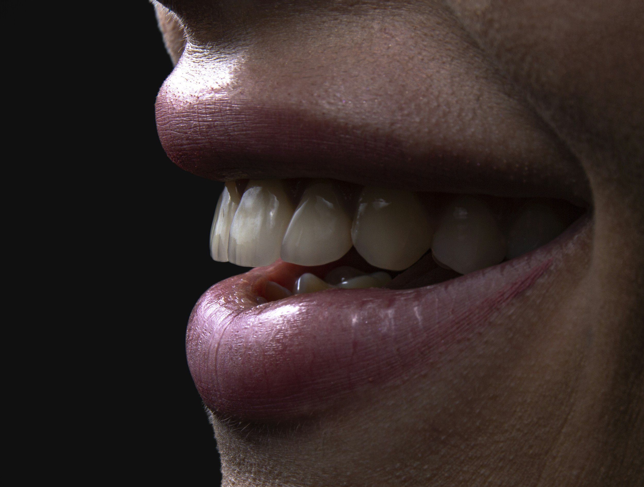 Close-up of a person's partially open mouth, showing teeth and lips, with dark background.