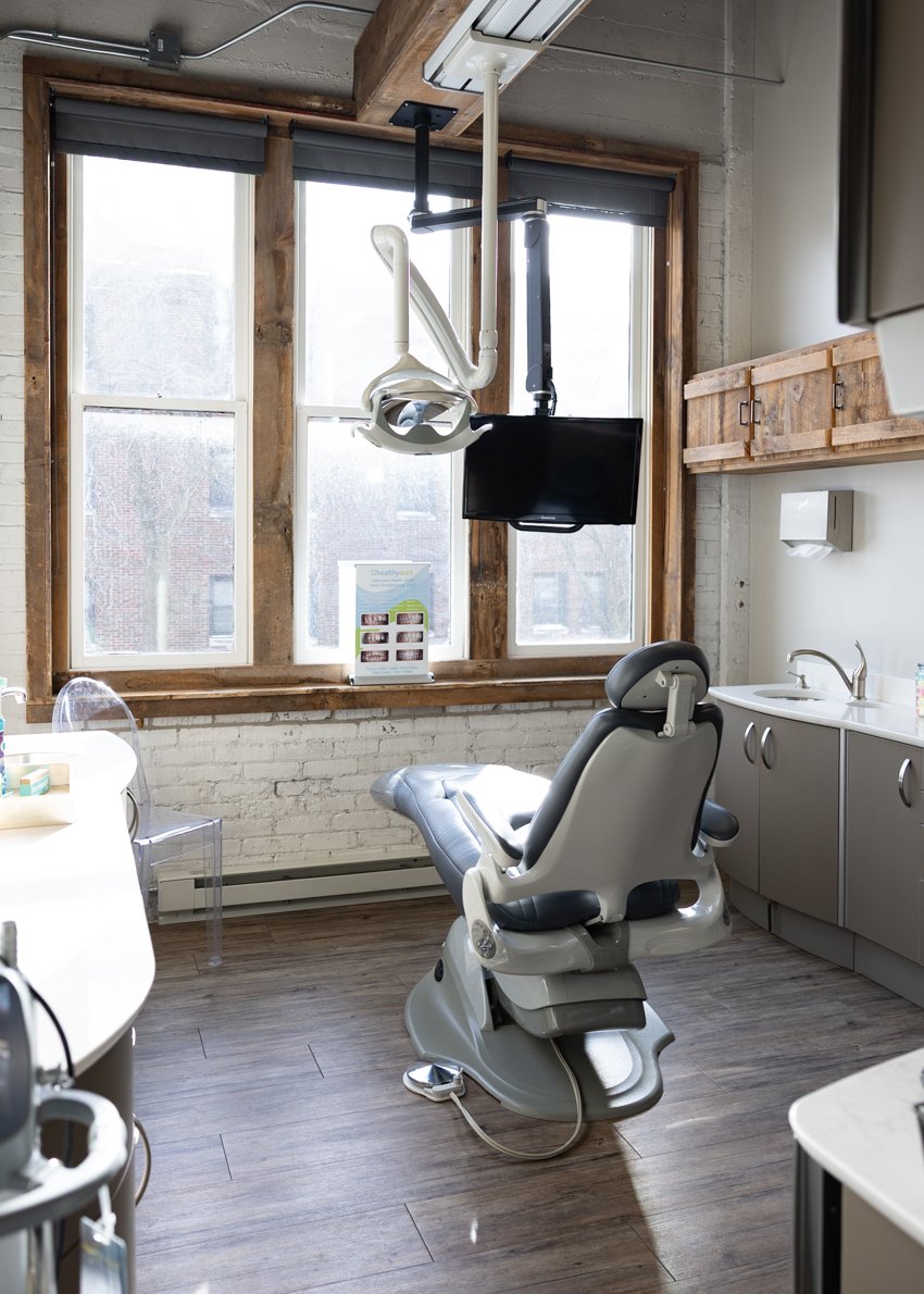 Dentist's office with dental chair, monitor, dental light, large window, and cabinets.