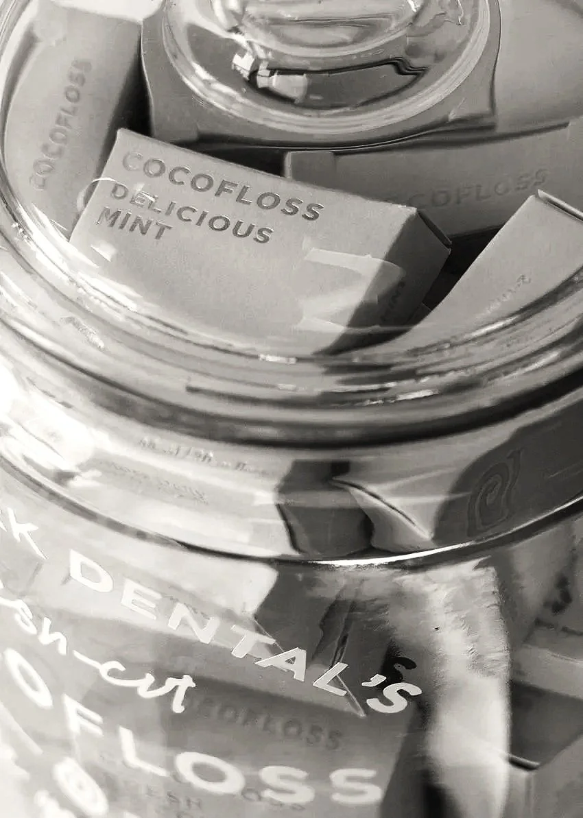 Close-up of a glass jar containing small white boxes labeled 'COCOFLOSS DELICIOUS MINT'.