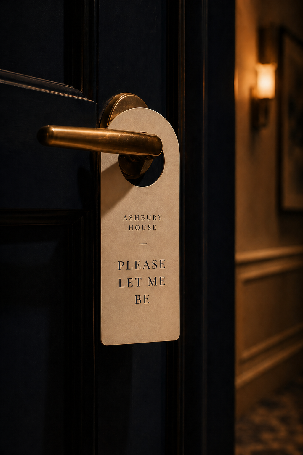 A door with a gold handle and a white door hanger sign that reads 'Ashbury House - Please Let Me Be' in black text.