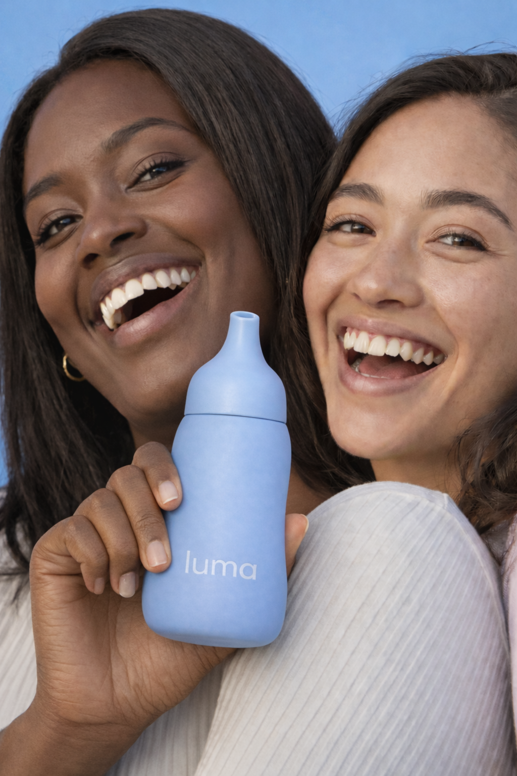Two happy women smiling and holding a blue Luma nasal spray bottle.