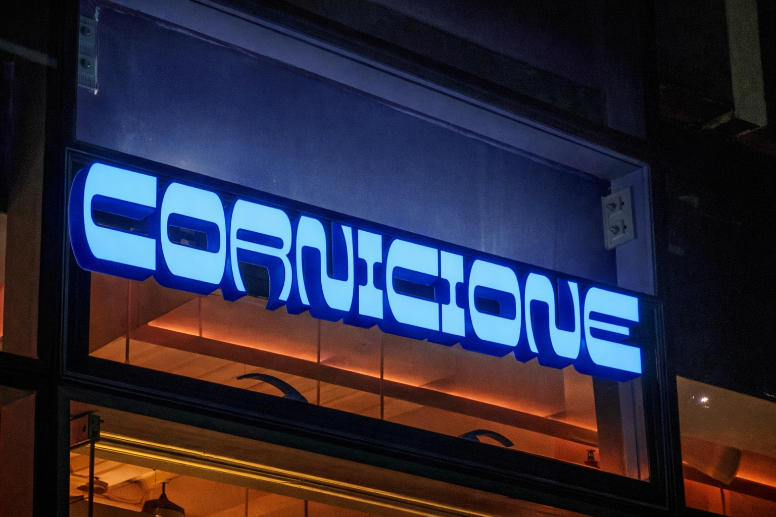 A blue illuminated sign that reads 'EDUCATION' in reverse, posted in a window at night, with a reflection of the sign visible inside the building.