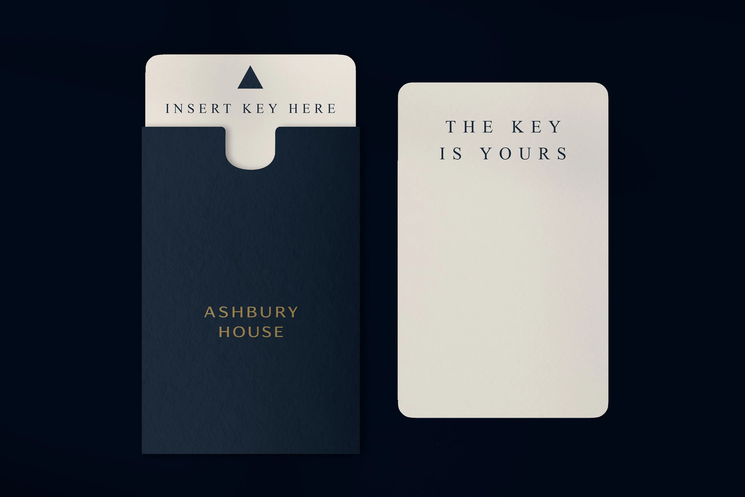 A card with the text 'INSERT KEY HERE' being inserted into a dark blue slot on a book titled 'Ashbury House'. Next to it is a white card with the text 'THE KEY IS YOURS'.