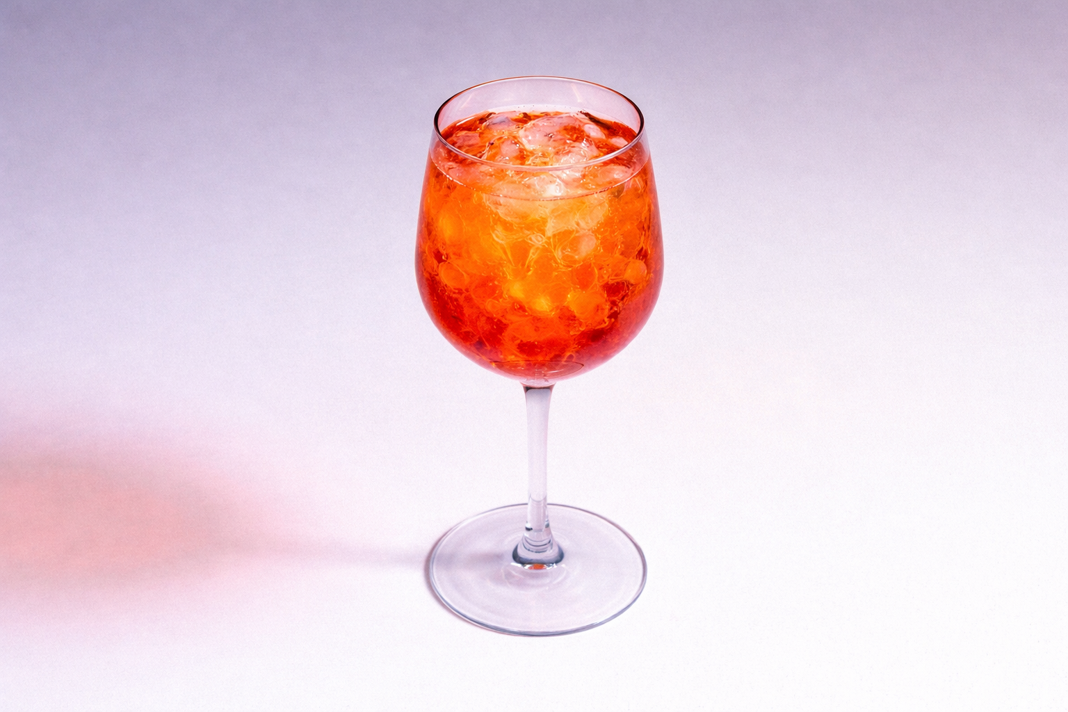 A wine glass filled with an orange-colored drink containing ice cubes.