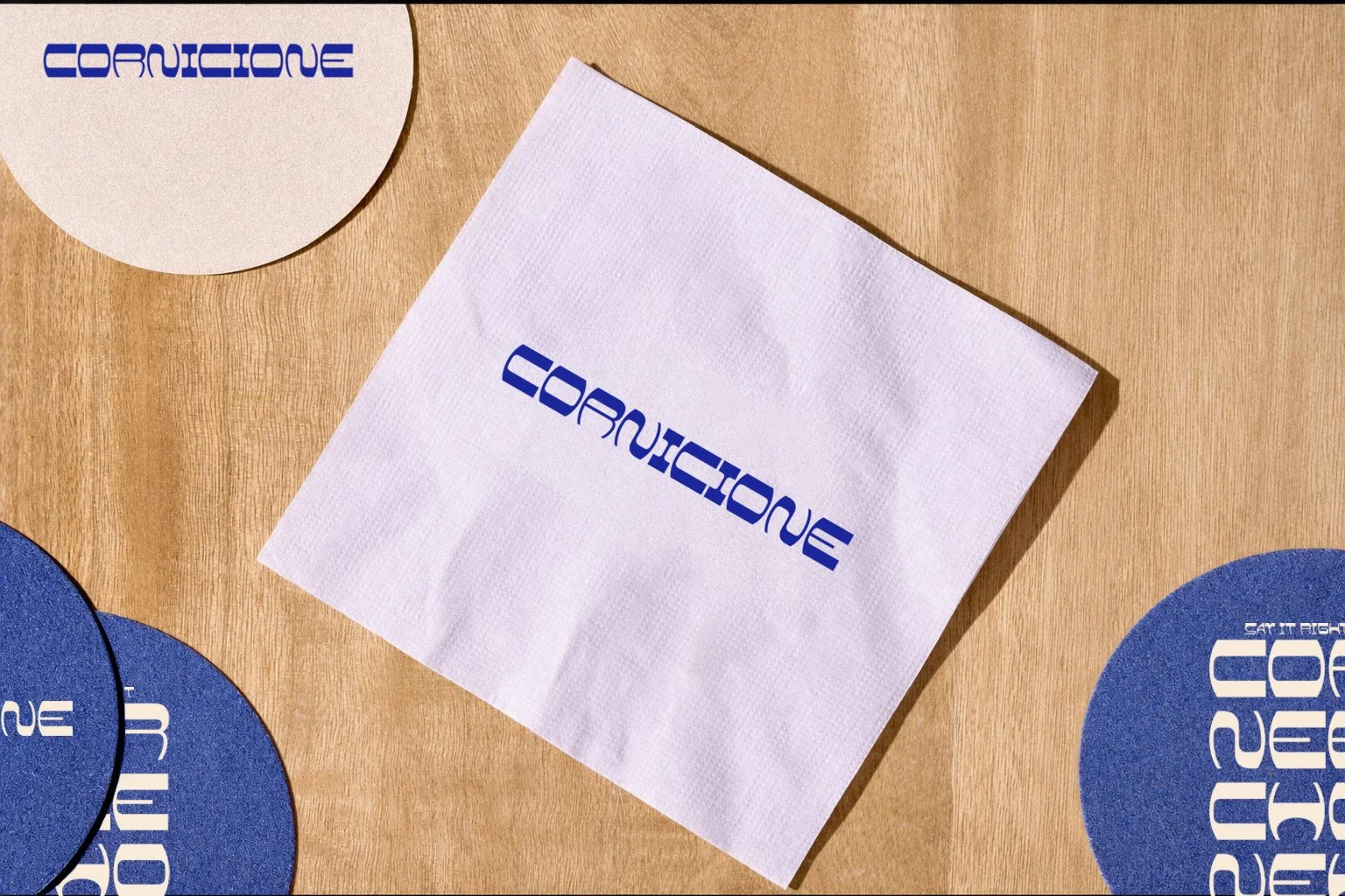Close-up of a wooden table with a white napkin and blue circular coasters all bearing the 'CORUCIQUE' logo in blue text.