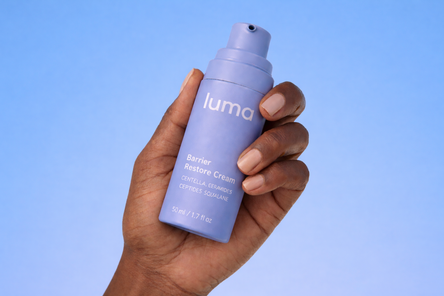 Hand holding a purple bottle labeled 'Luma Barrier Restore Cream' against a blue background.
