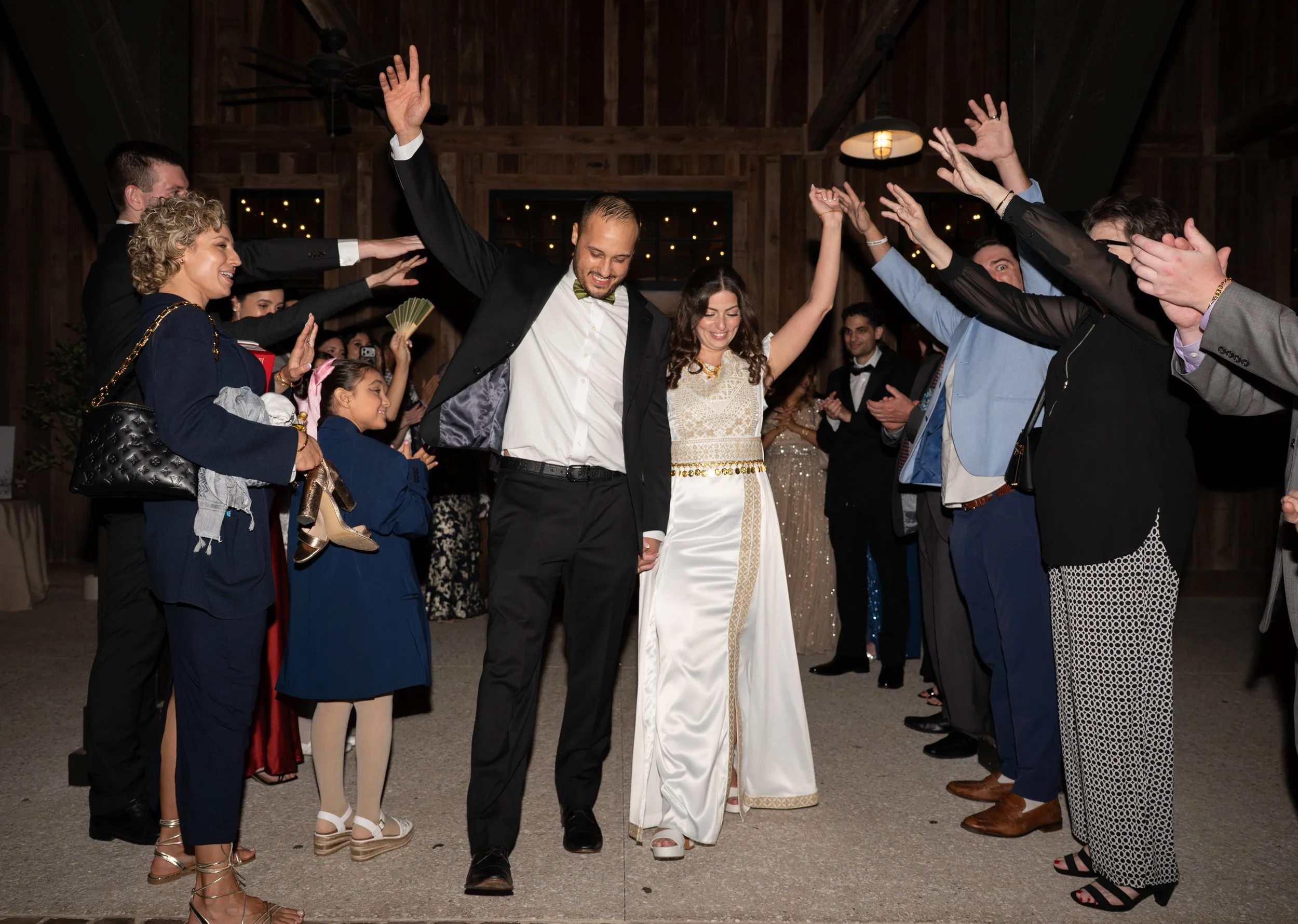 A group of people celebrating at a wedding reception, dancing and smiling with a wooden interior background.