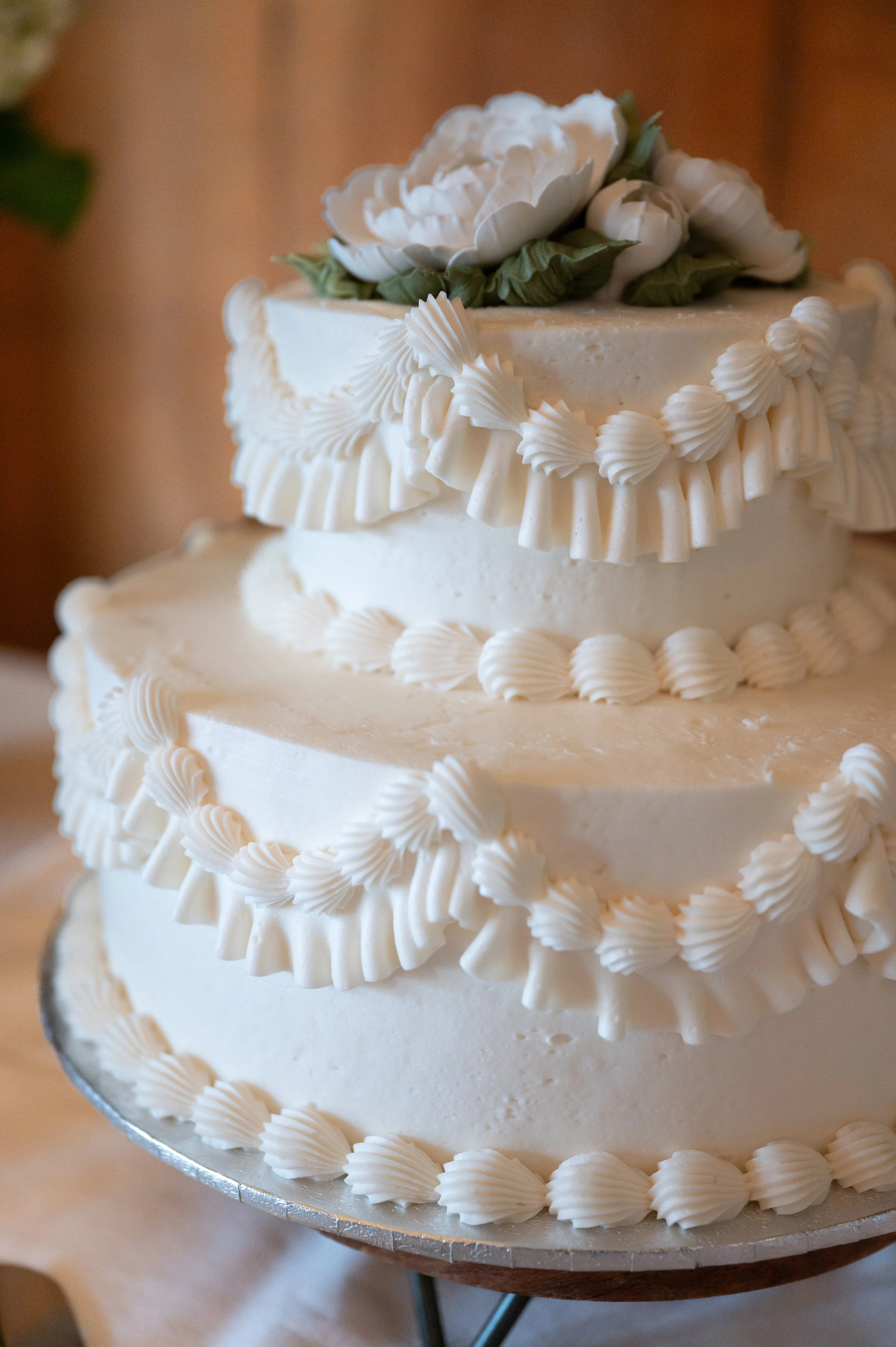 A multi-tiered white wedding cake decorated with piped frosting and topped with white flowers and green leaves.