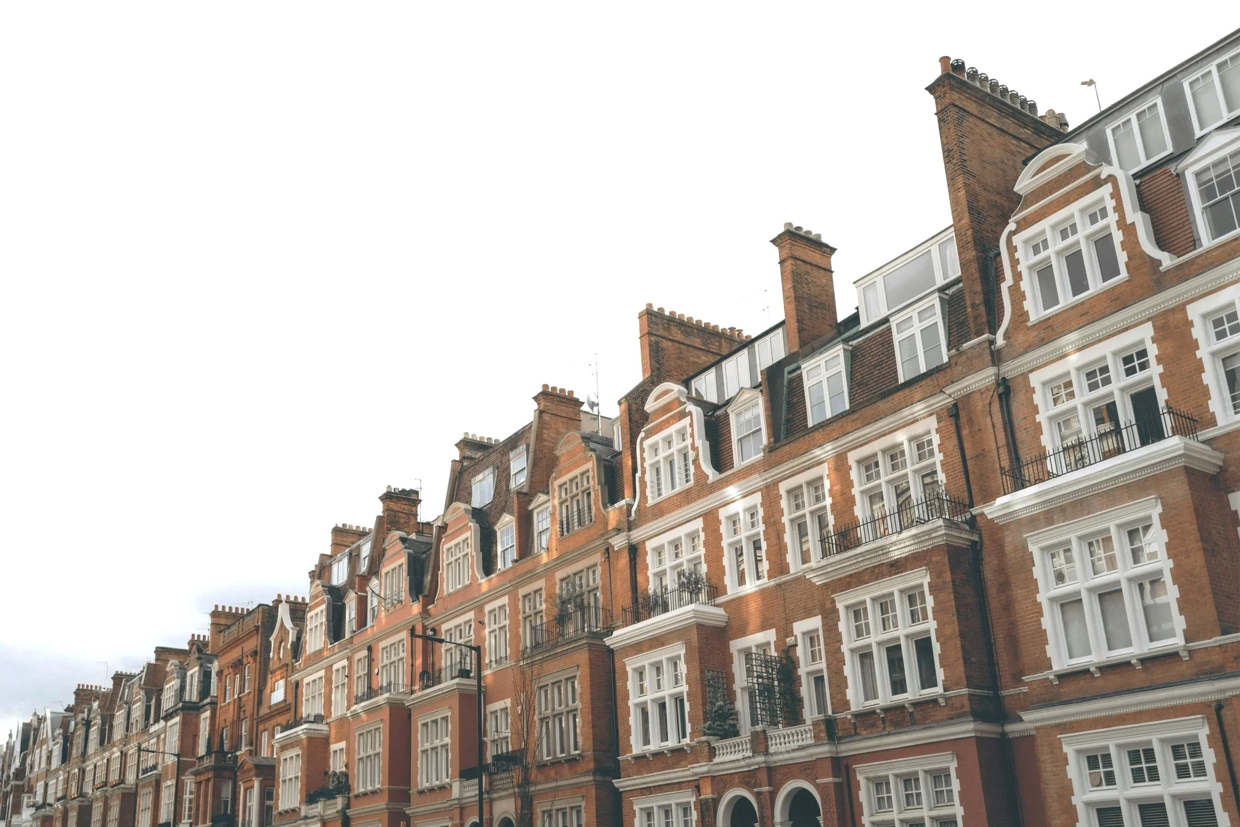 Row of red brick residential buildings with white window frames and black balconies, under an overcast sky.