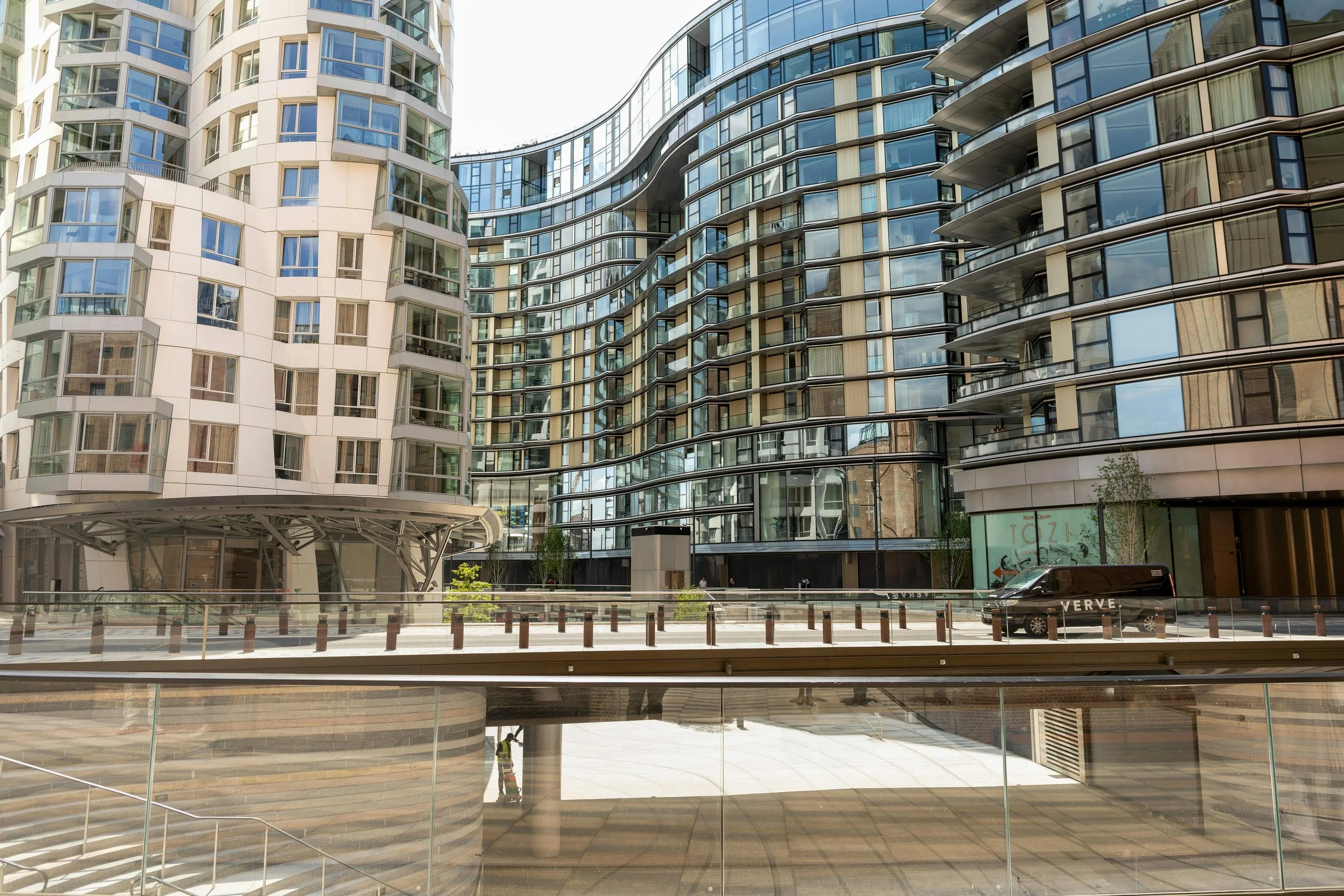 Modern multi-story residential buildings with glass facades and balconies, seen from an outdoor plaza with stairs and railing.