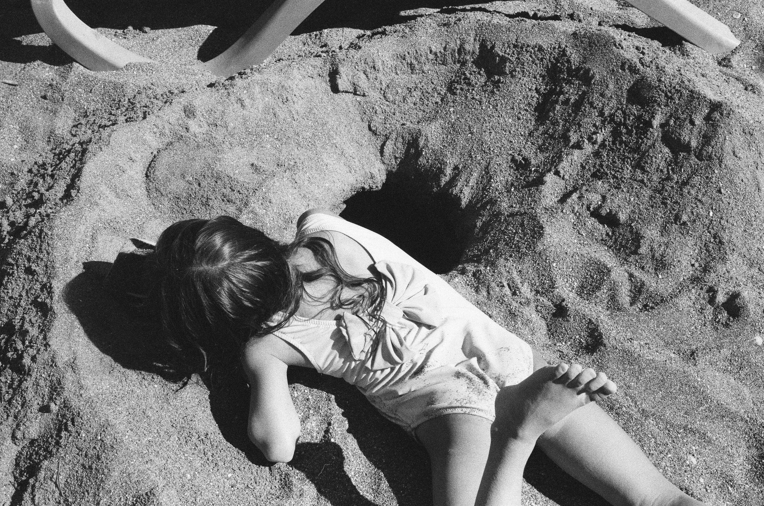 Child lying face down in sand, exterior scene