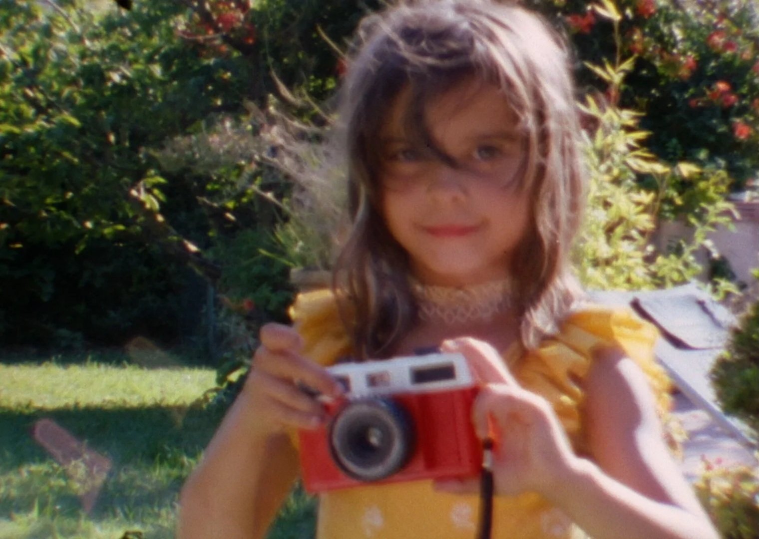 Girl in garden smiles with camera in hand