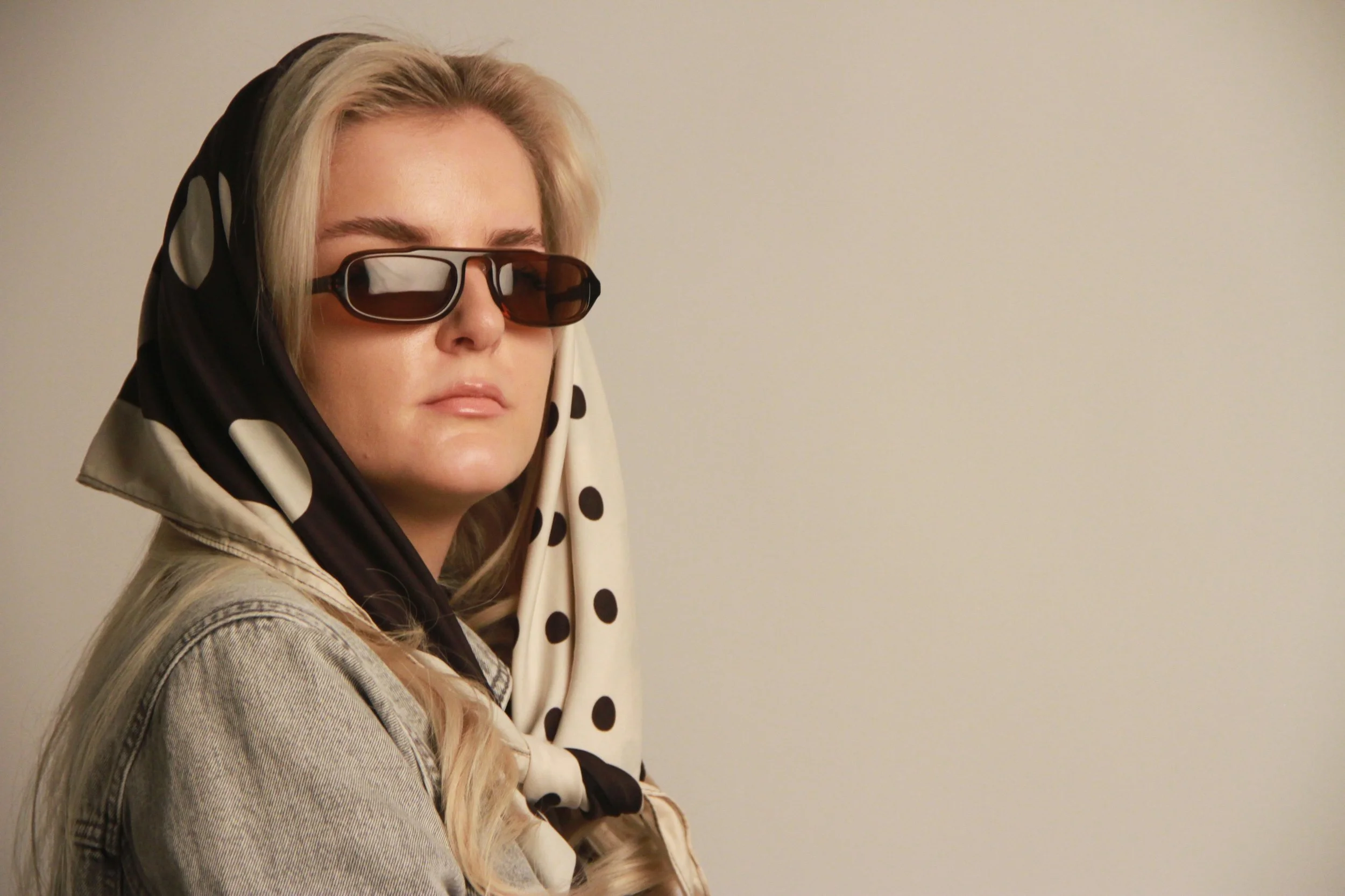 Gjeneta wearing a patterned headscarf and sunglasses in a contemporary studio editorial portrait.