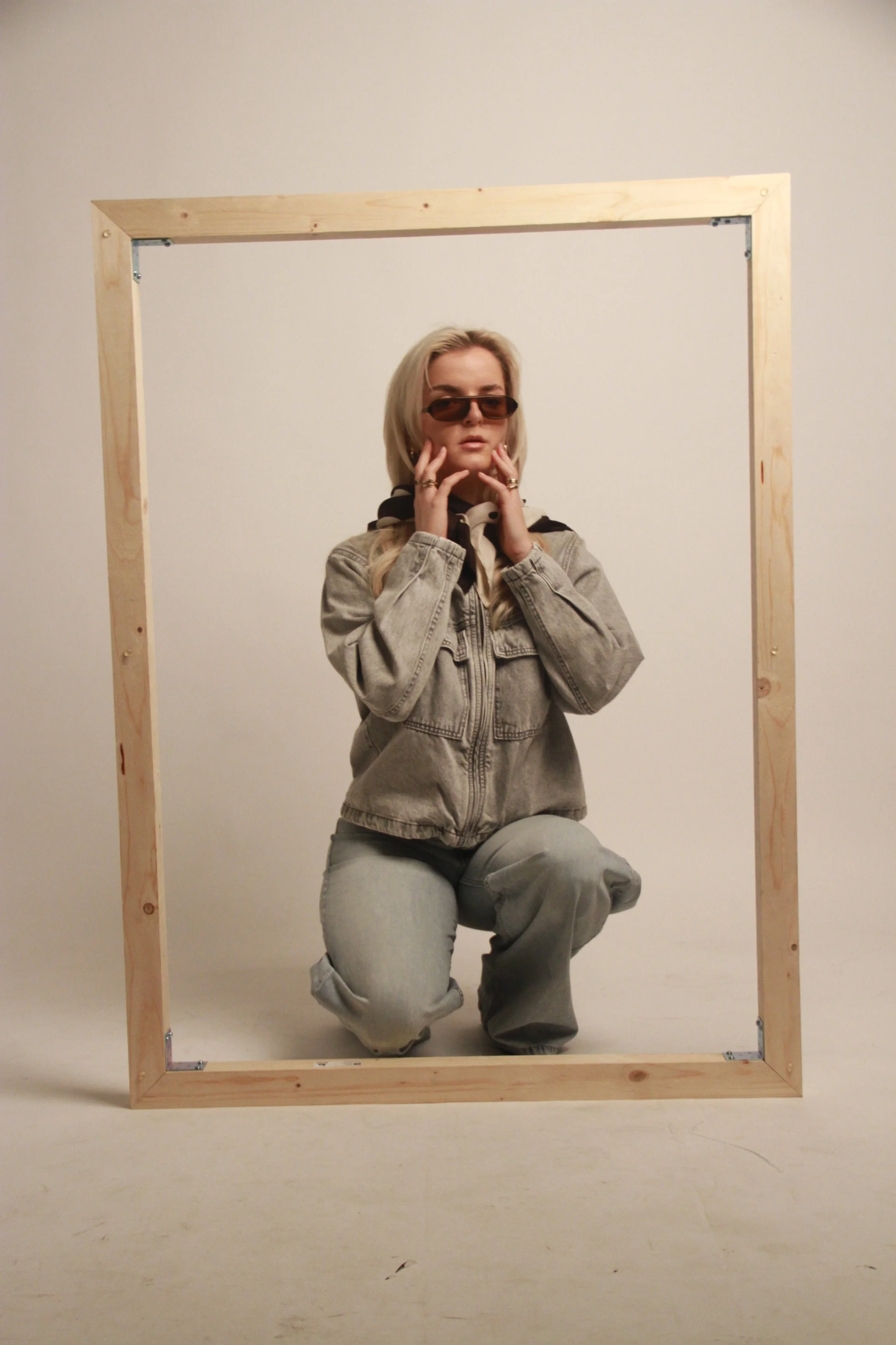 Gjeneta kneeling within a wooden frame in studio, exploring containment and identity in editorial portrait photography.