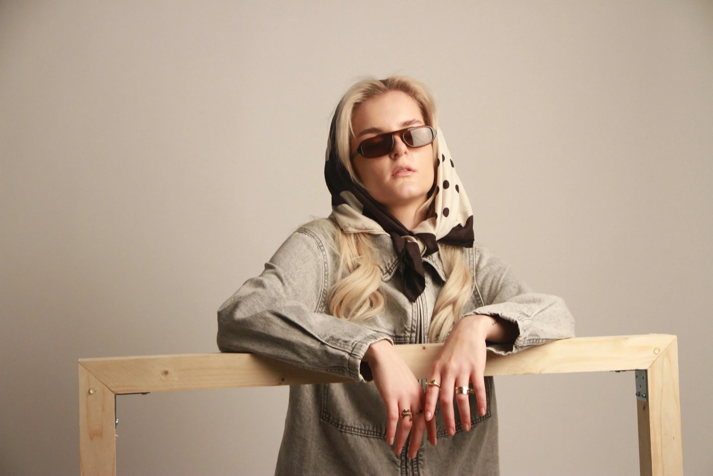 Gjeneta leaning over a wooden frame in a minimal studio setting, conceptual editorial portrait.