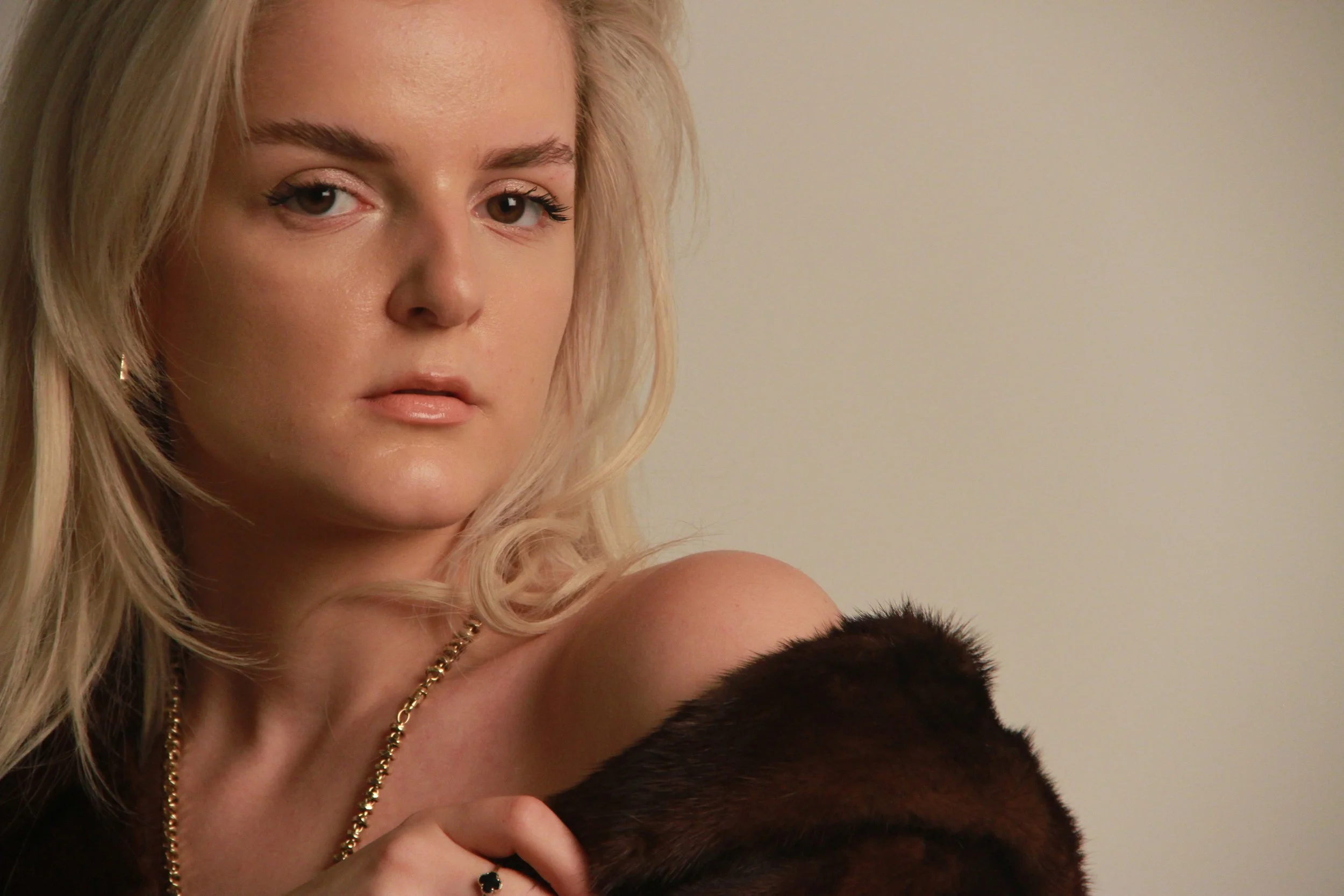 Close-up portrait of Gjeneta with fur draped over her shoulder, neutral background and restrained editorial styling.