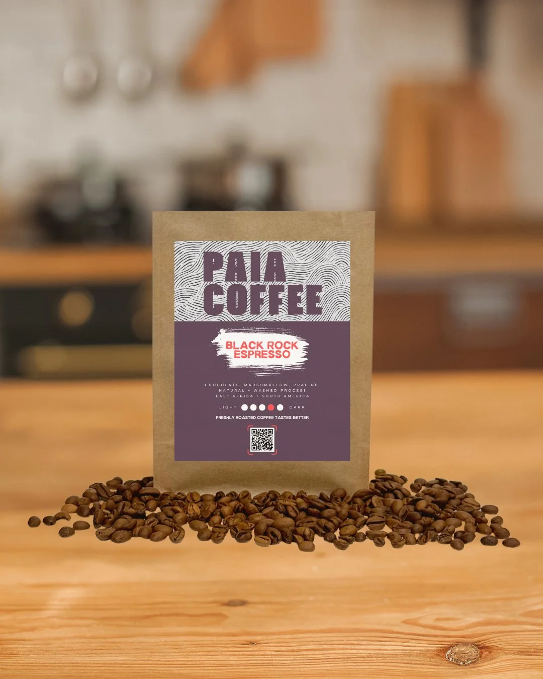 A bag of PAIA Coffee Black Rock Espresso surrounded by coffee beans on a wooden table in a kitchen setting.