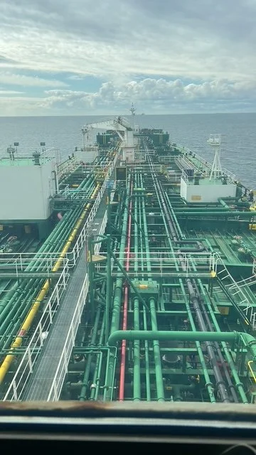 View of a ship's deck with various pipelines, machinery, and equipment, extending toward the horizon over the ocean with cloudy sky.