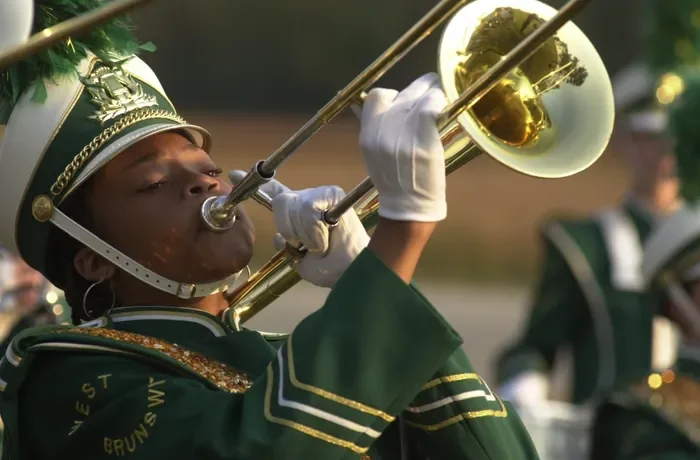 A marching band member in a green uniform with gold accents playing a trumpet.