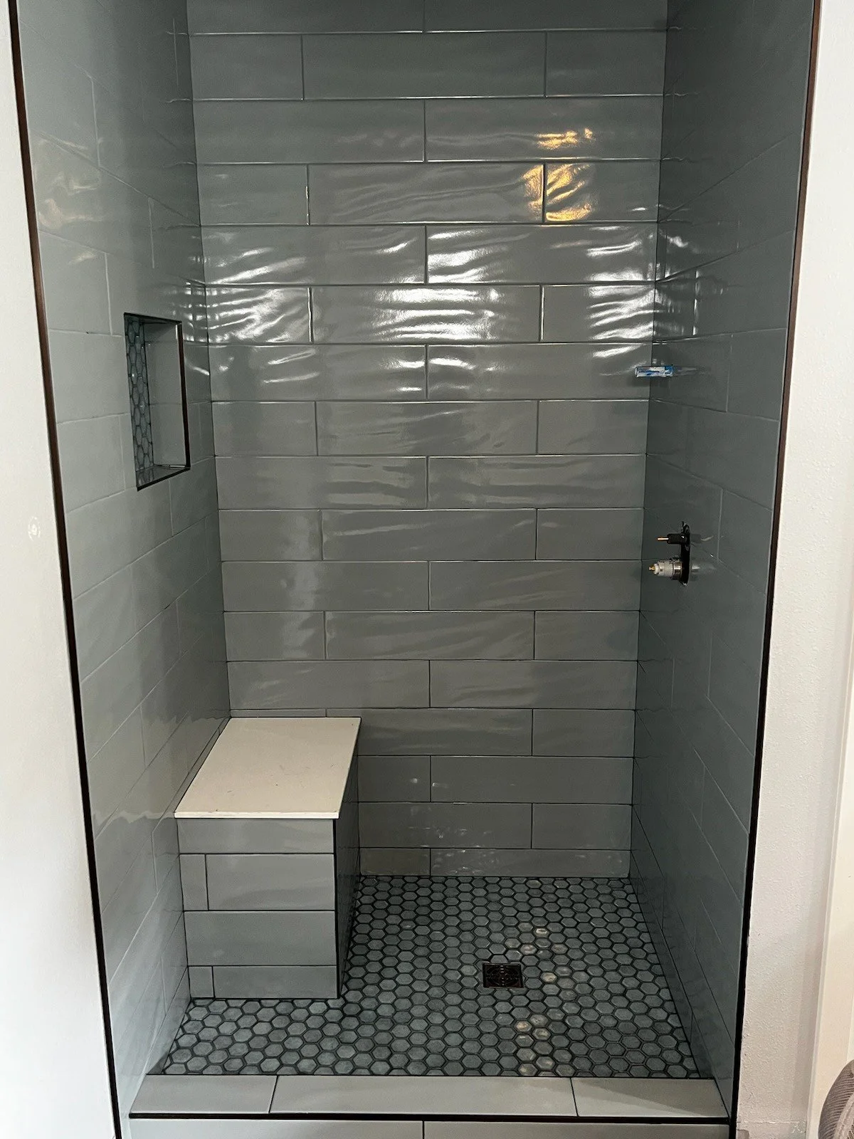 Empty walk-in shower with gray subway tile walls, a small built-in bench, a niche with patterned tile, and a drain on the floor.