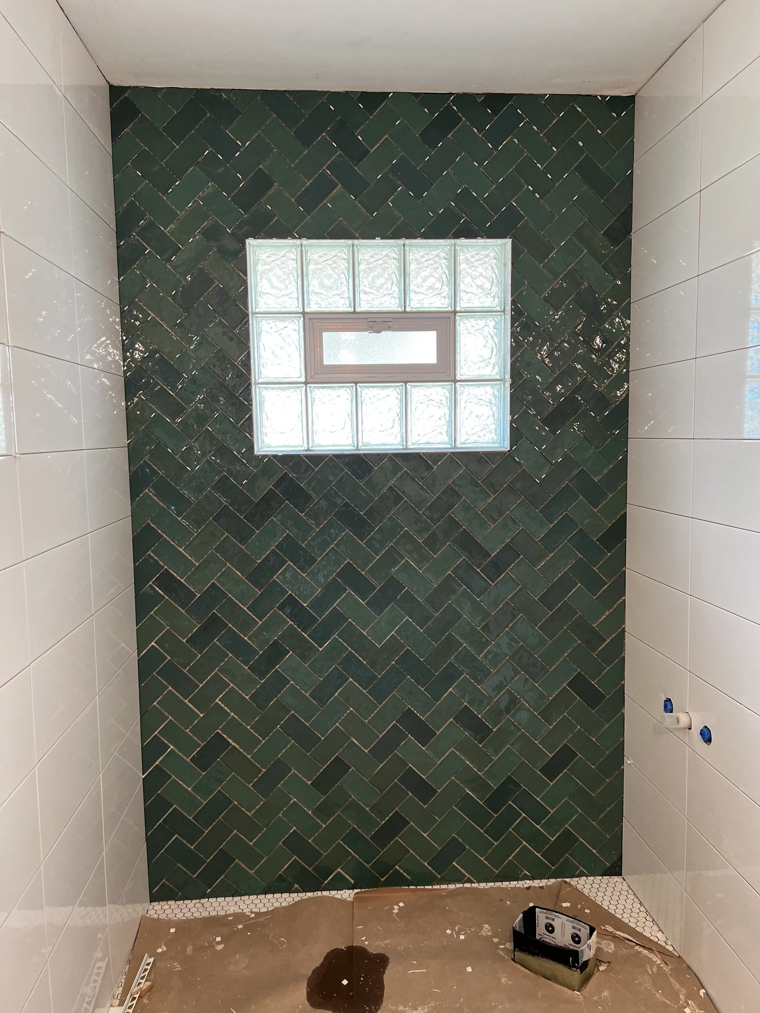 Bathroom with green herringbone tiled accent wall and glass block window, white tiled walls on the sides, and plumbing fixtures for a shower or bathtub installation.