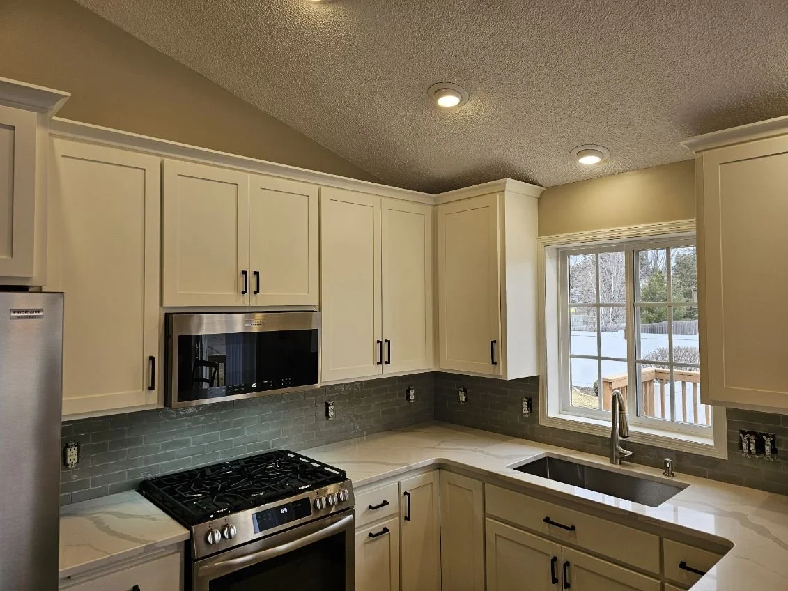 Kitchen with white cabinets, a stainless steel microwave, a gas stove, a dynamic gray subway tile backsplash, and a window above the sink with a view of a backyard.
