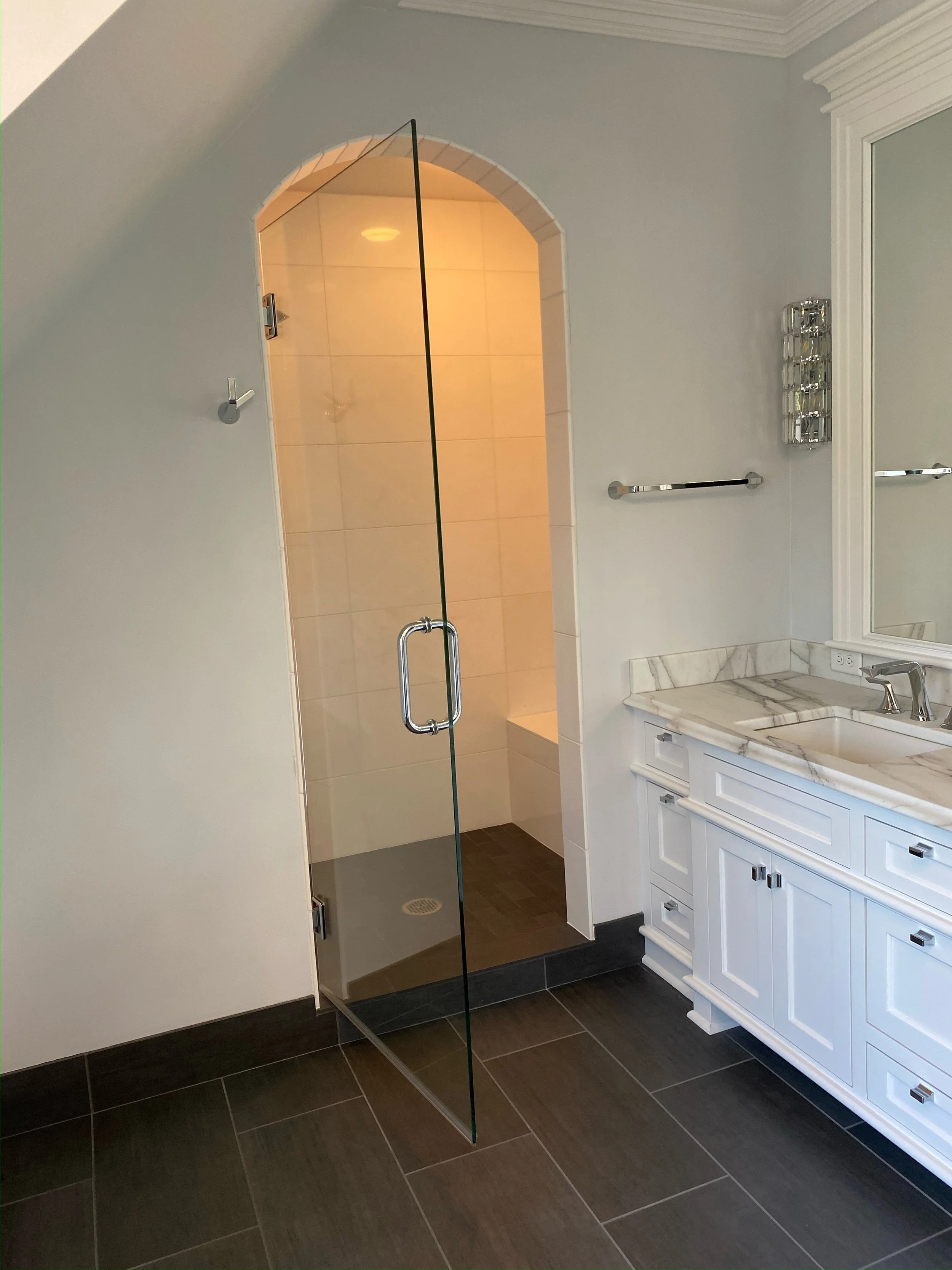 A bathroom with a glass shower enclosure, white cabinet with marble countertop, and a large mirror.