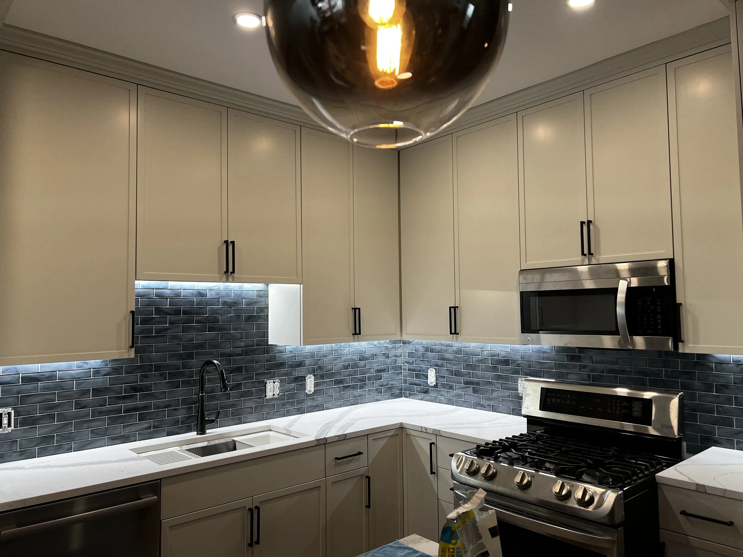Modern kitchen with white cabinets, black handles, a black subway tile backsplash, a stainless steel microwave, a stainless steel gas stove, and a white marble countertop with a black sink and black faucet.