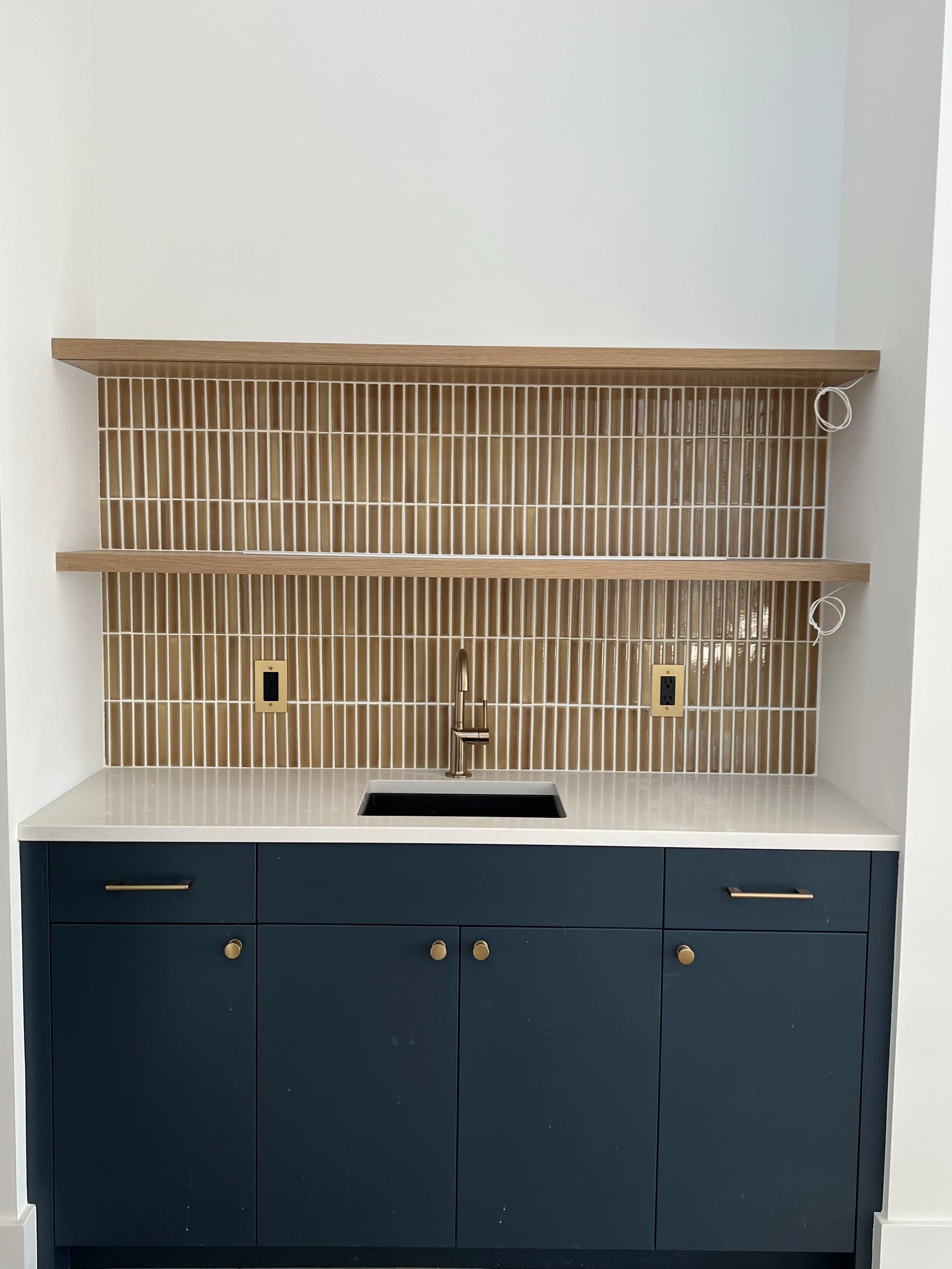 Kitchen sink with dark blue cabinets, beige tile backsplash, open shelving, and an empty countertop.