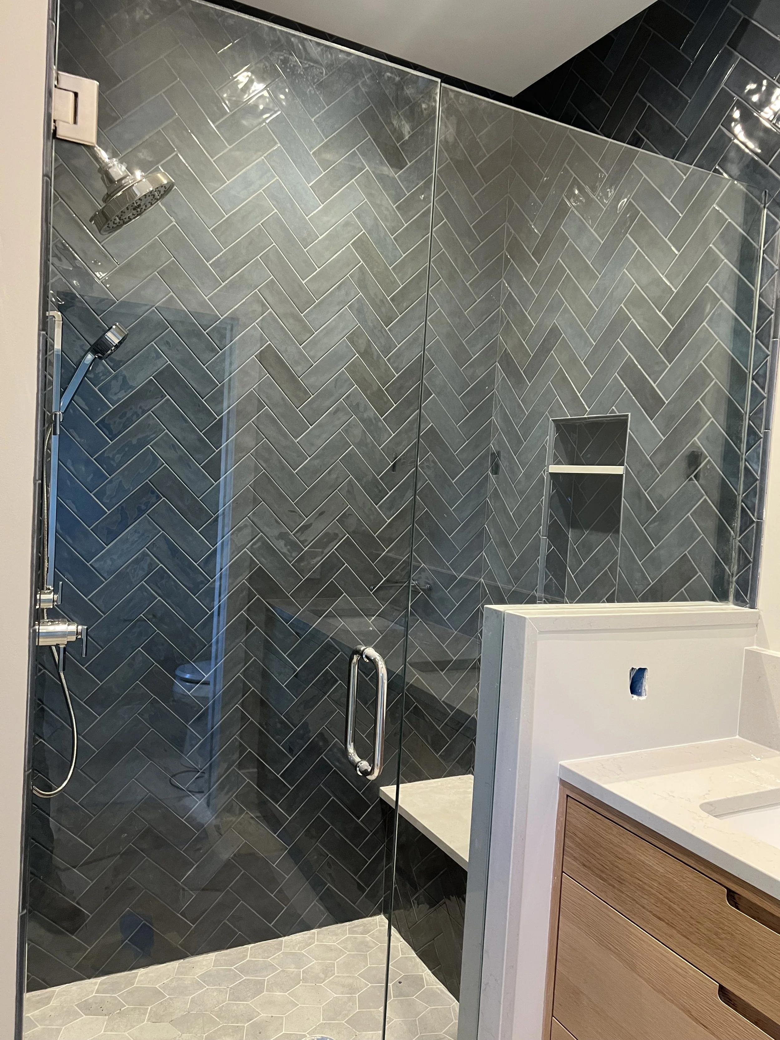Modern bathroom shower with black herringbone tile walls, glass enclosure, and built-in niche with shelf.