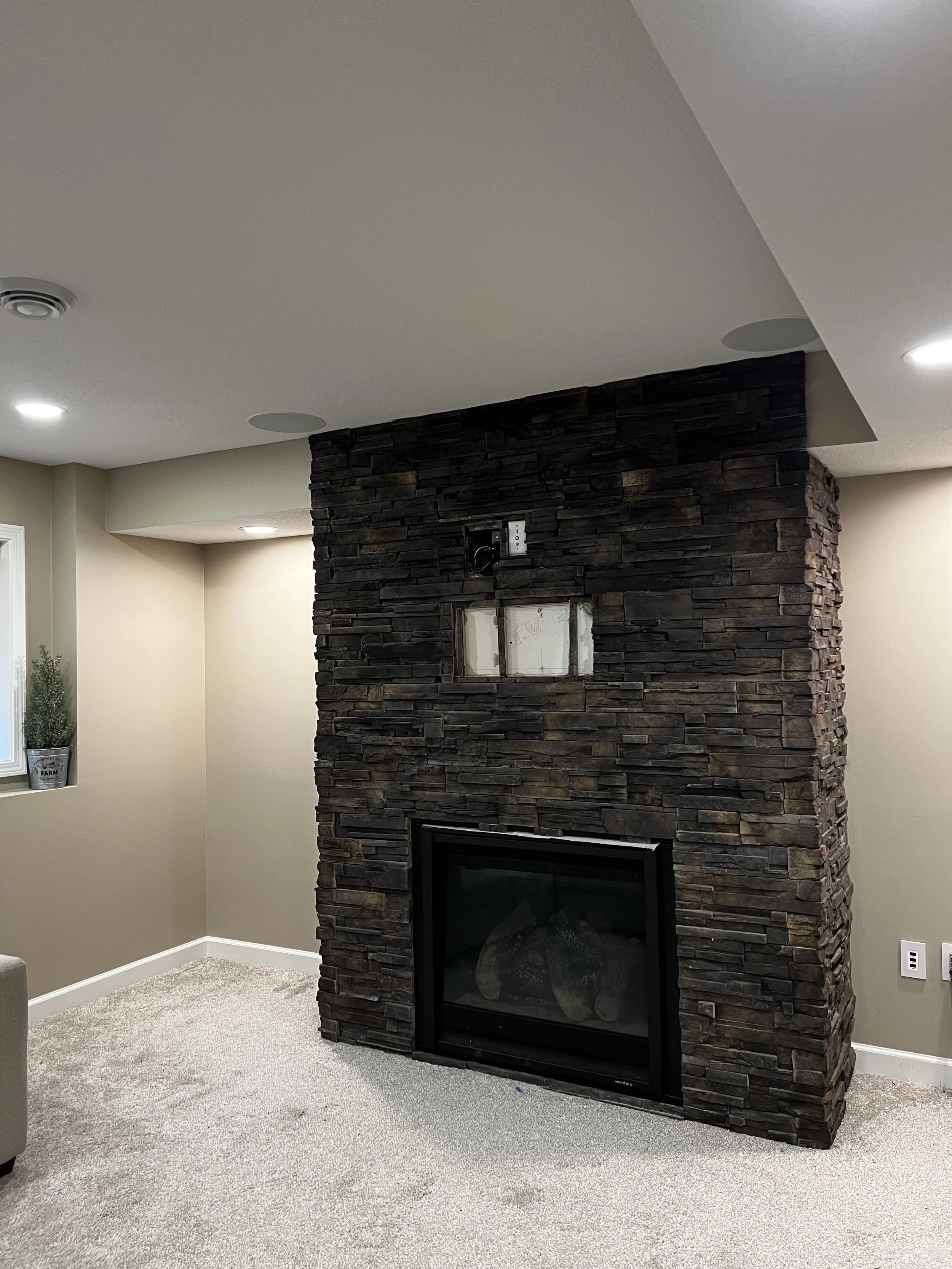 Modern living room with a stacked stone fireplace and built-in firebox, beige walls, and carpeted floor.