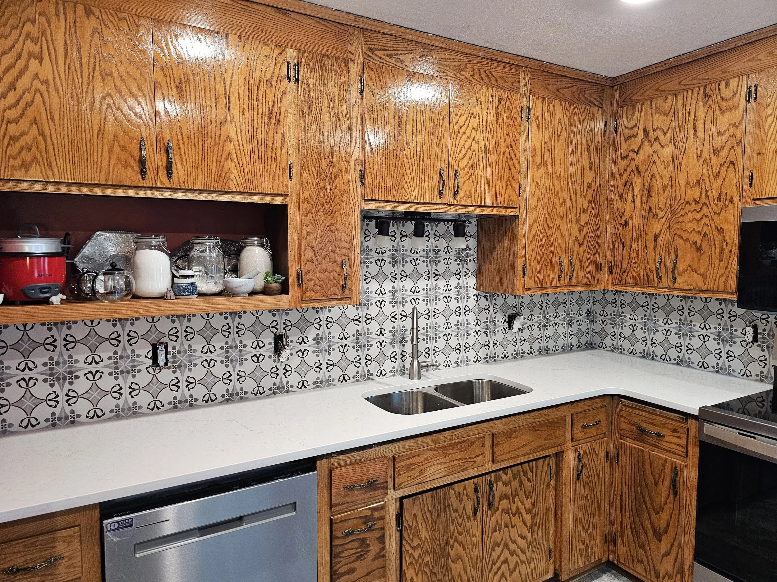 Kitchen with wooden cabinets, patterned tile backsplash, double sink, and white countertops.