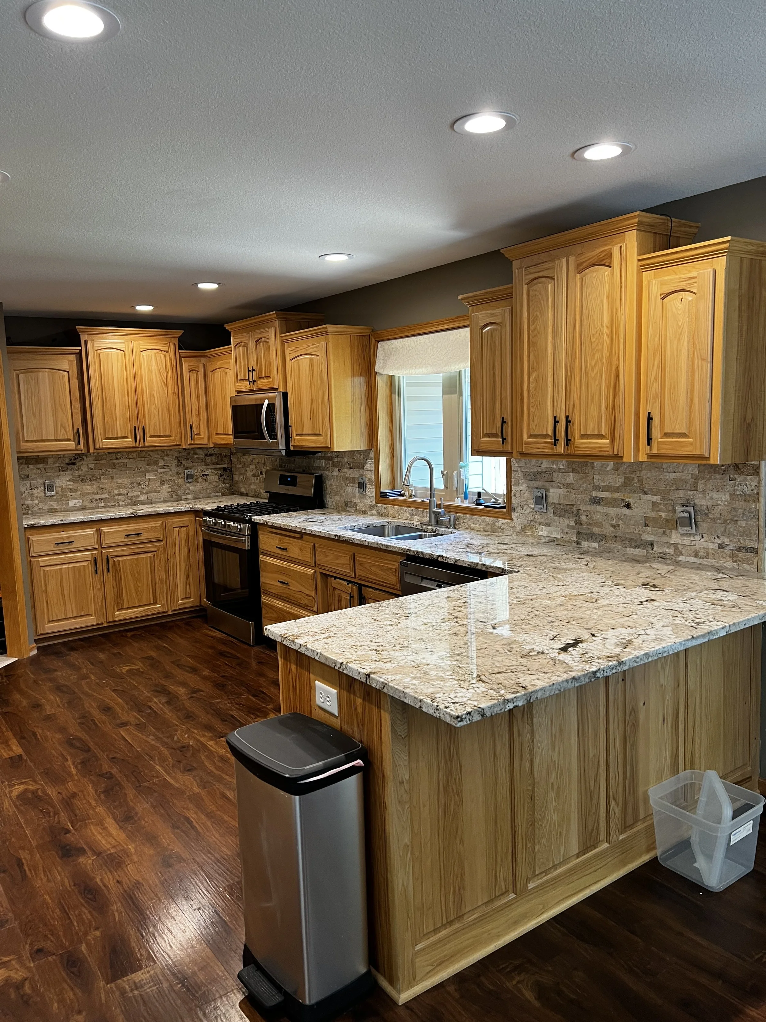 Kitchen with wooden cabinets, granite countertops, stainless steel appliances, hardwood floors, and a window above the sink.